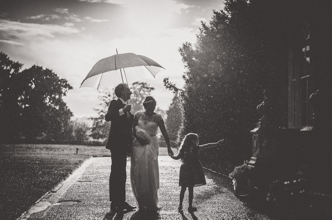 A wedding photo capturing the groom and bride under an umbrella in the rain.