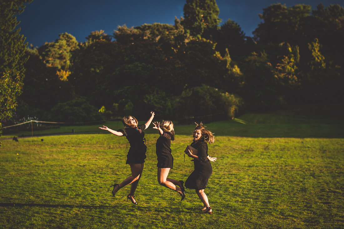 Three brides jumping in the air on a grassy field, captured by a wedding photographer.
