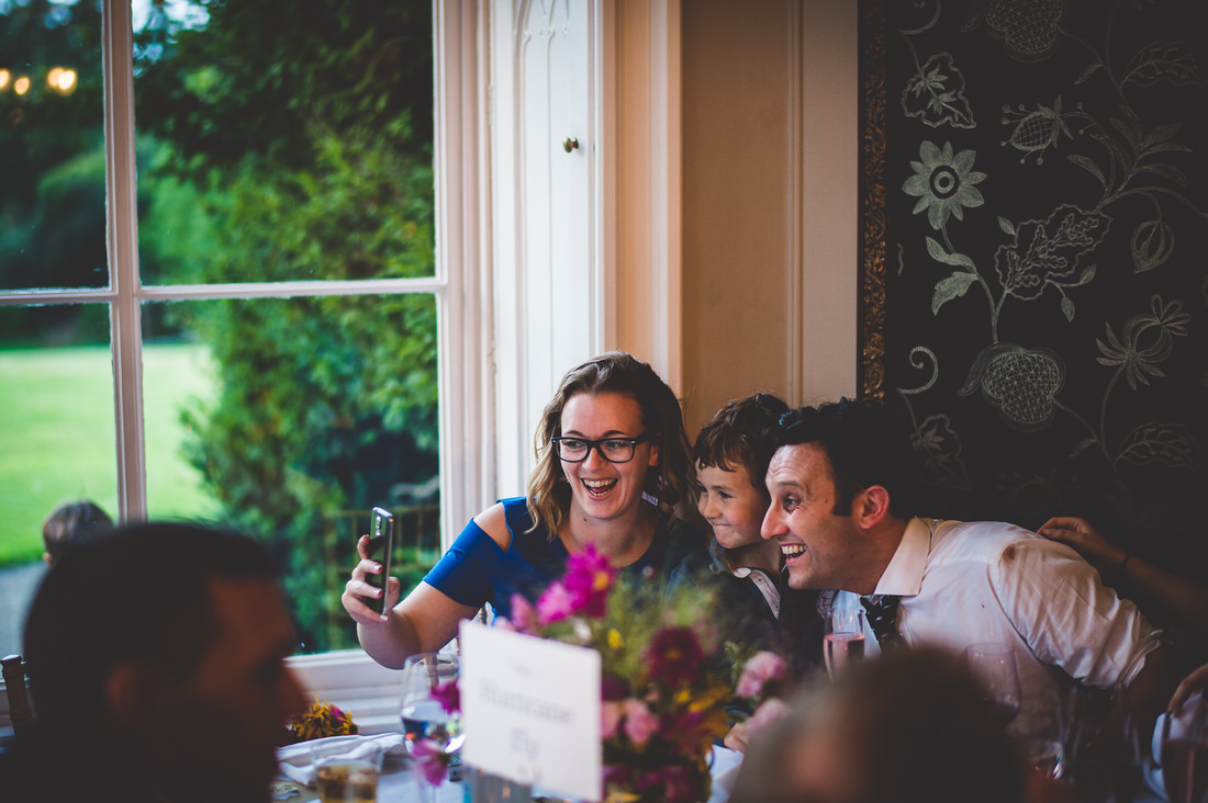 A wedding photographer capturing a group selfie at a reception.