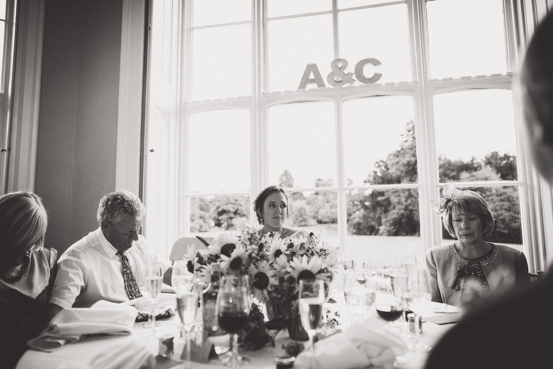 A black and white photo of a wedding party sitting at a table, captured by a wedding photographer.