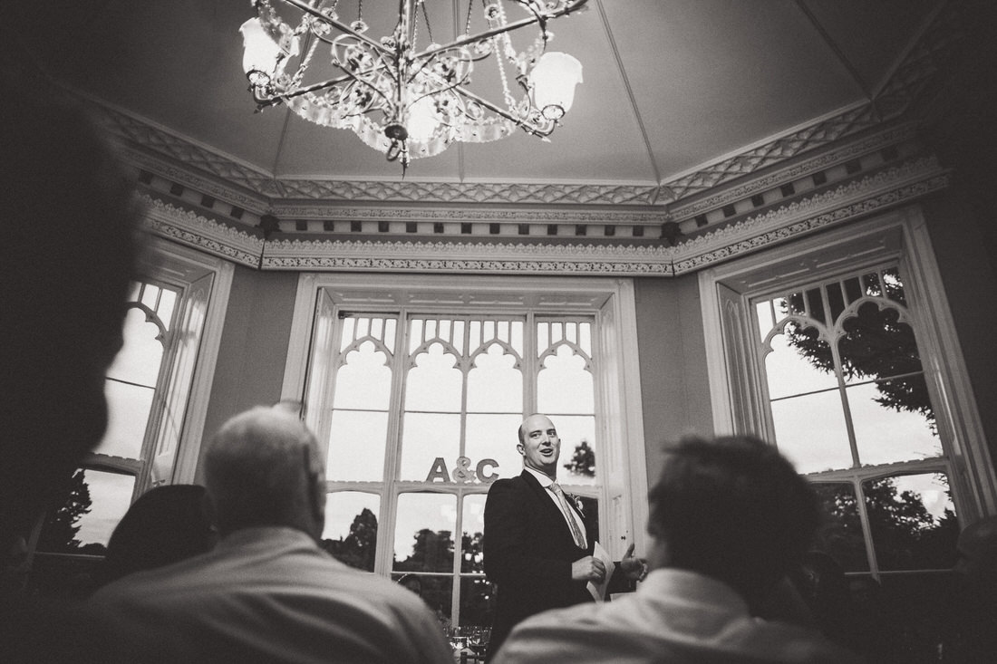 A groom delivering a speech during the wedding reception under a grand chandelier.