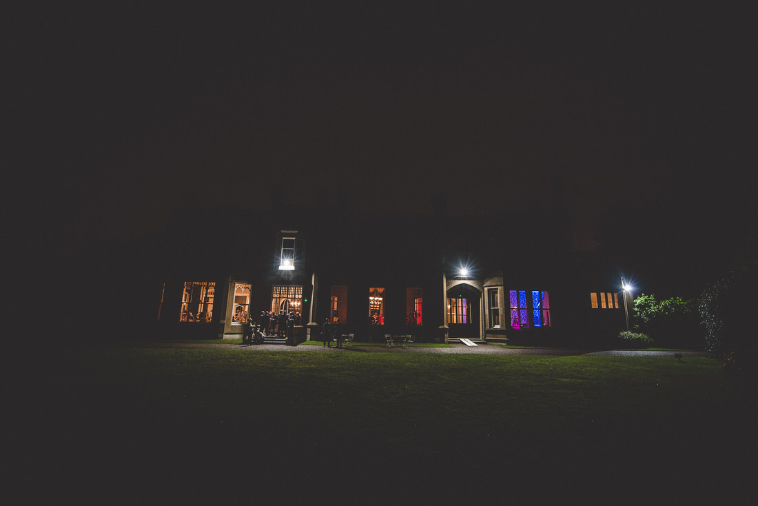 A stunning wedding venue, with a grand house sparkling with lights at night, captured by a skilled wedding photographer.
