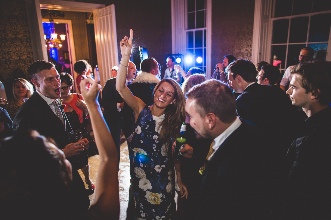 A wedding photographer captures the bride and guests dancing at a wedding reception.