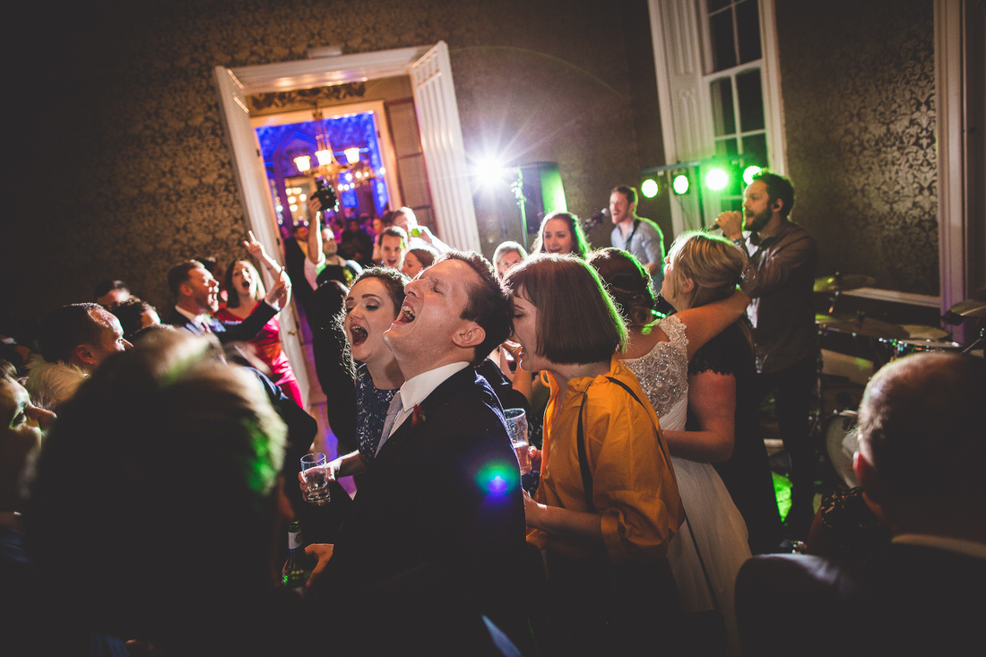 A wedding photographer captures a group of people dancing at a wedding reception.