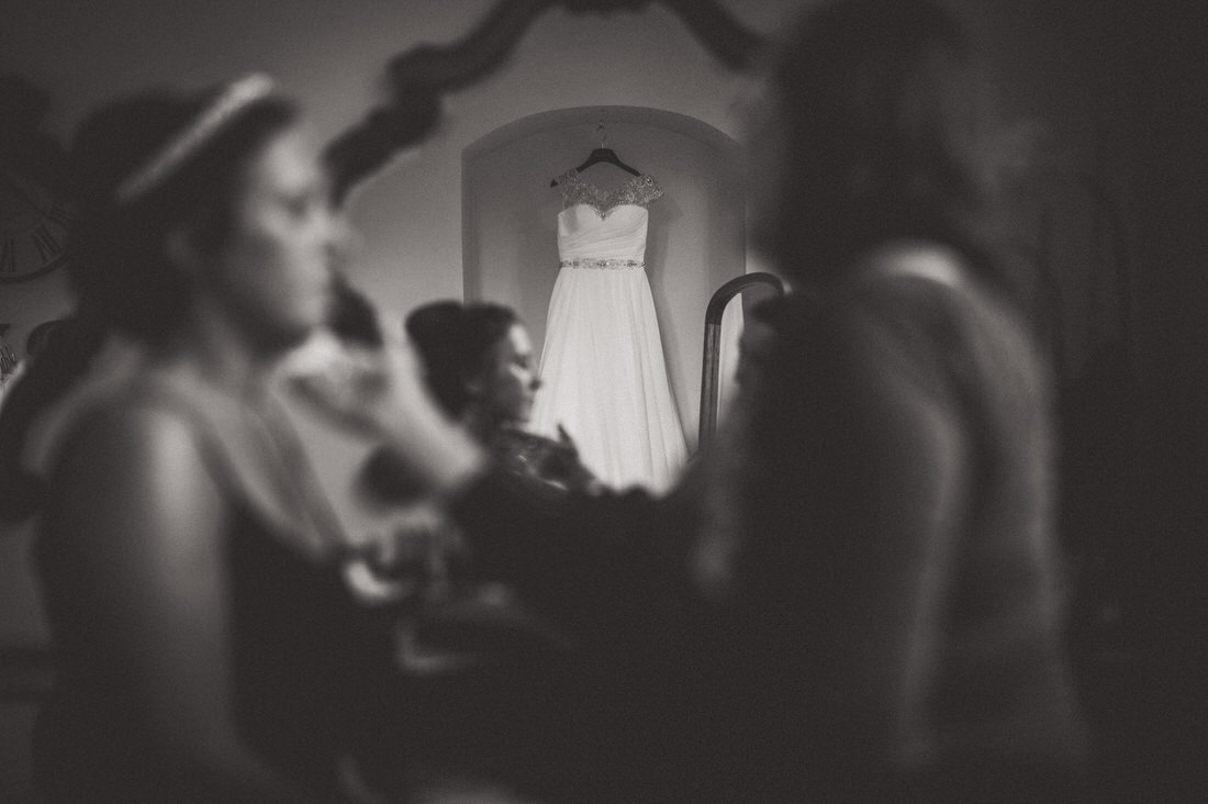 A bride is getting ready for her wedding day, with the help of a mirror and a wedding photographer.