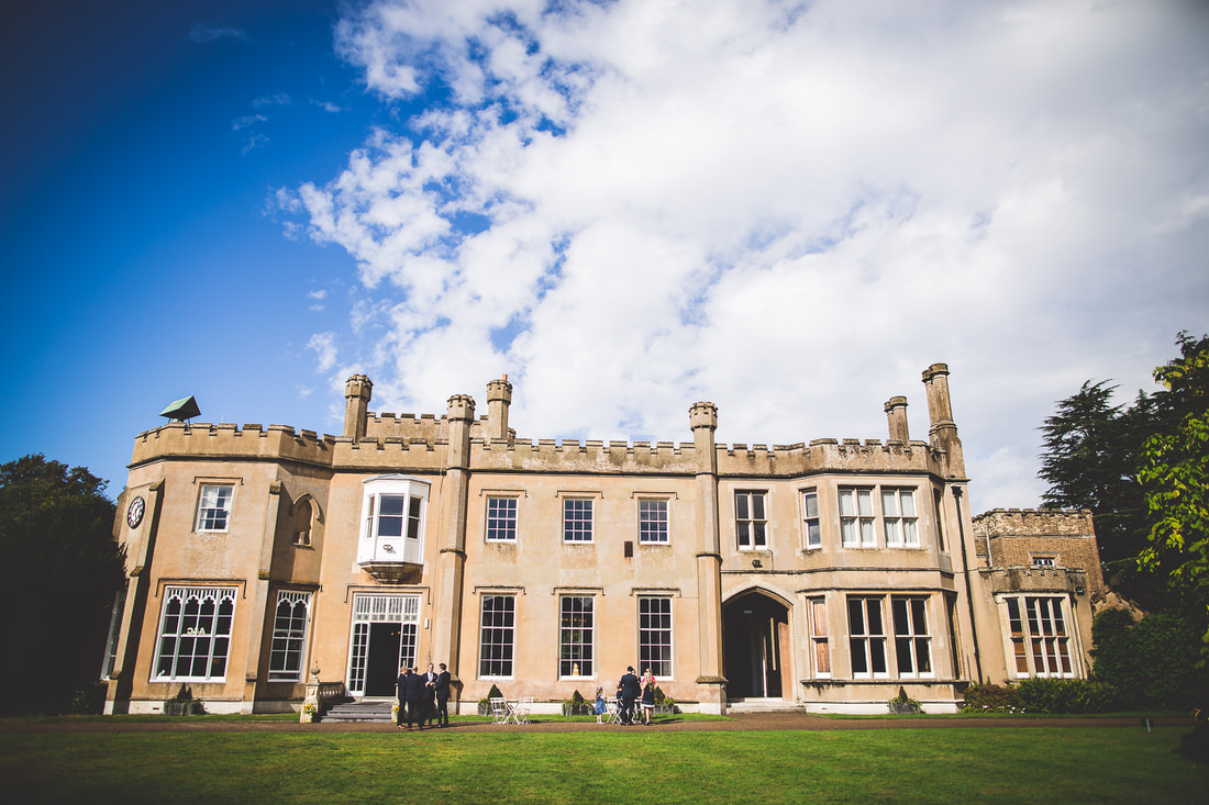 A grand mansion with a group of people, including a bride and a wedding photographer, standing outside.