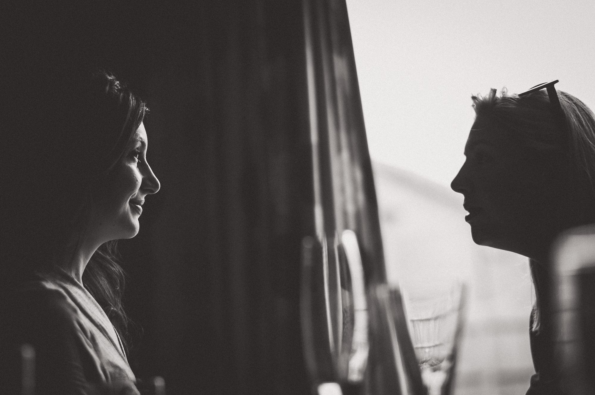 Two women sharing a tender moment as a wedding photographer captures their gaze through the window.