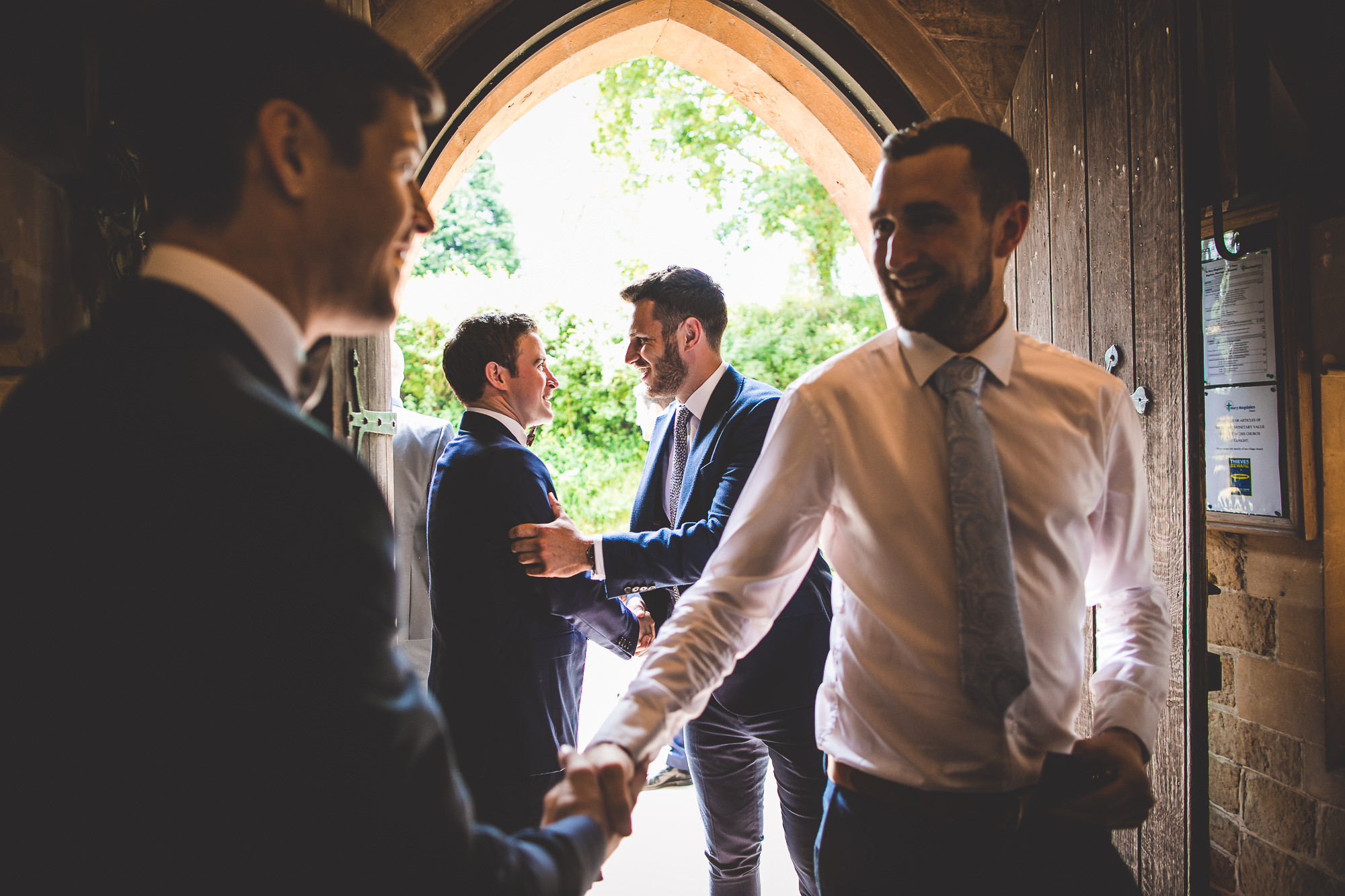 A groom and his best man shaking hands in a doorway, captured in a wedding photo.