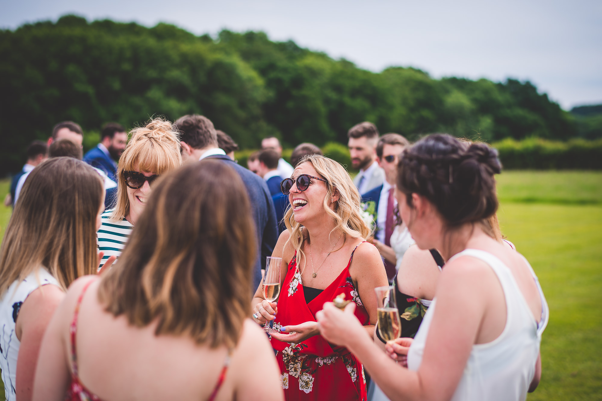 A group of people drinking wine in a field during a wedding photo session.