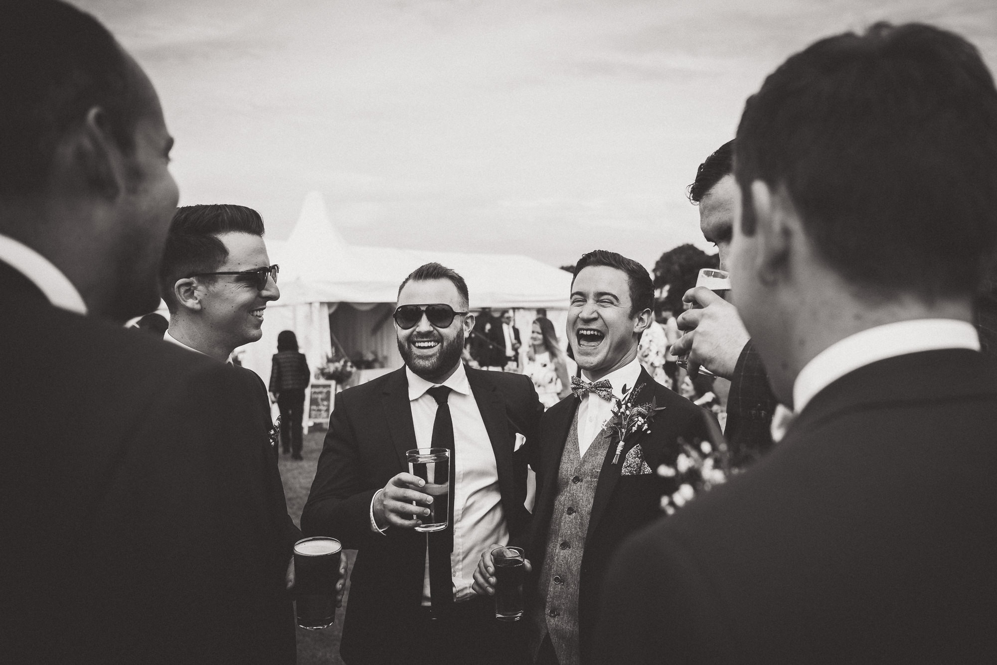 A wedding photographer captures a group of groomsmen laughing.