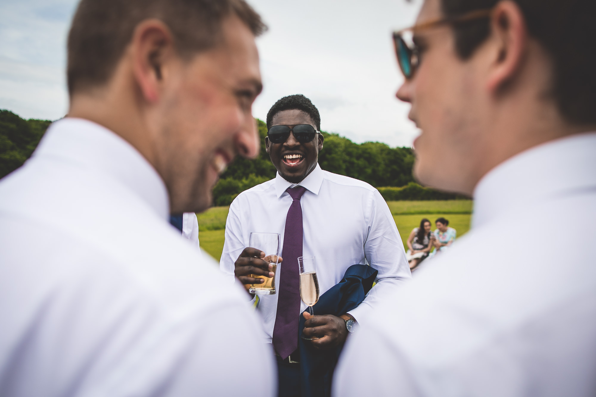 A group of men are laughing at each other in a field during a wedding photo.