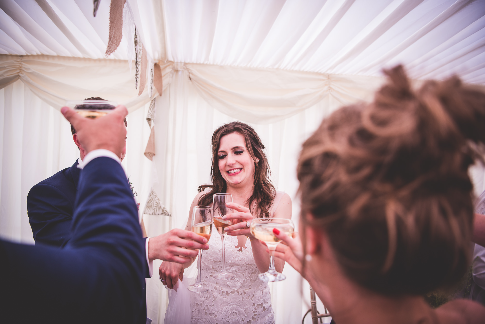 A wedding photographer capturing the bride and groom toasting champagne in a tent.