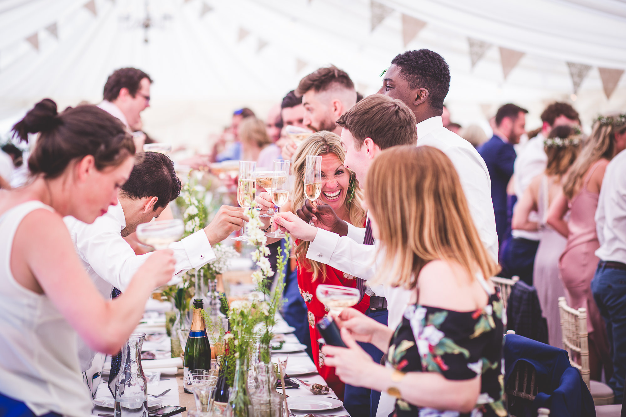 A groom and bride along with their wedding party toasting at a tented wedding reception.