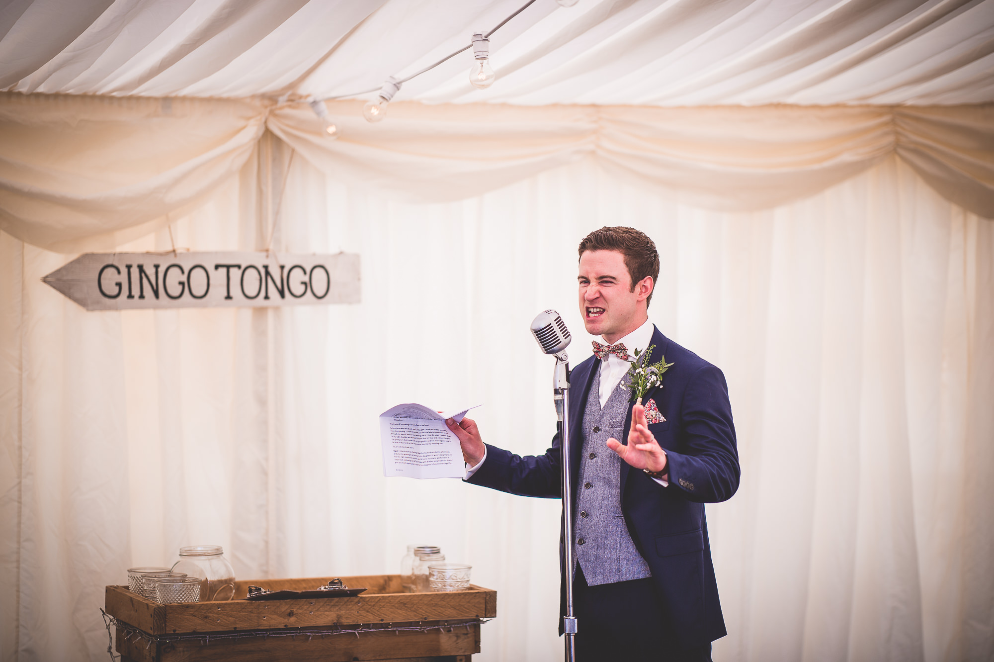 A groom in a suit speaking into a microphone during a wedding.