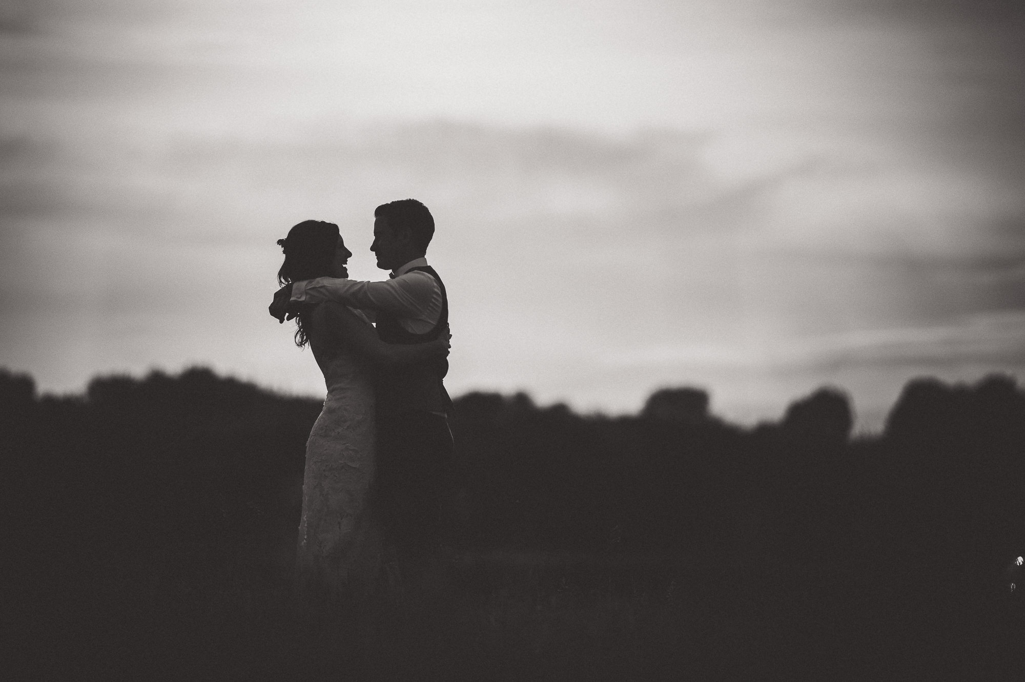 A wedding photo of a bride and groom embracing in a field.