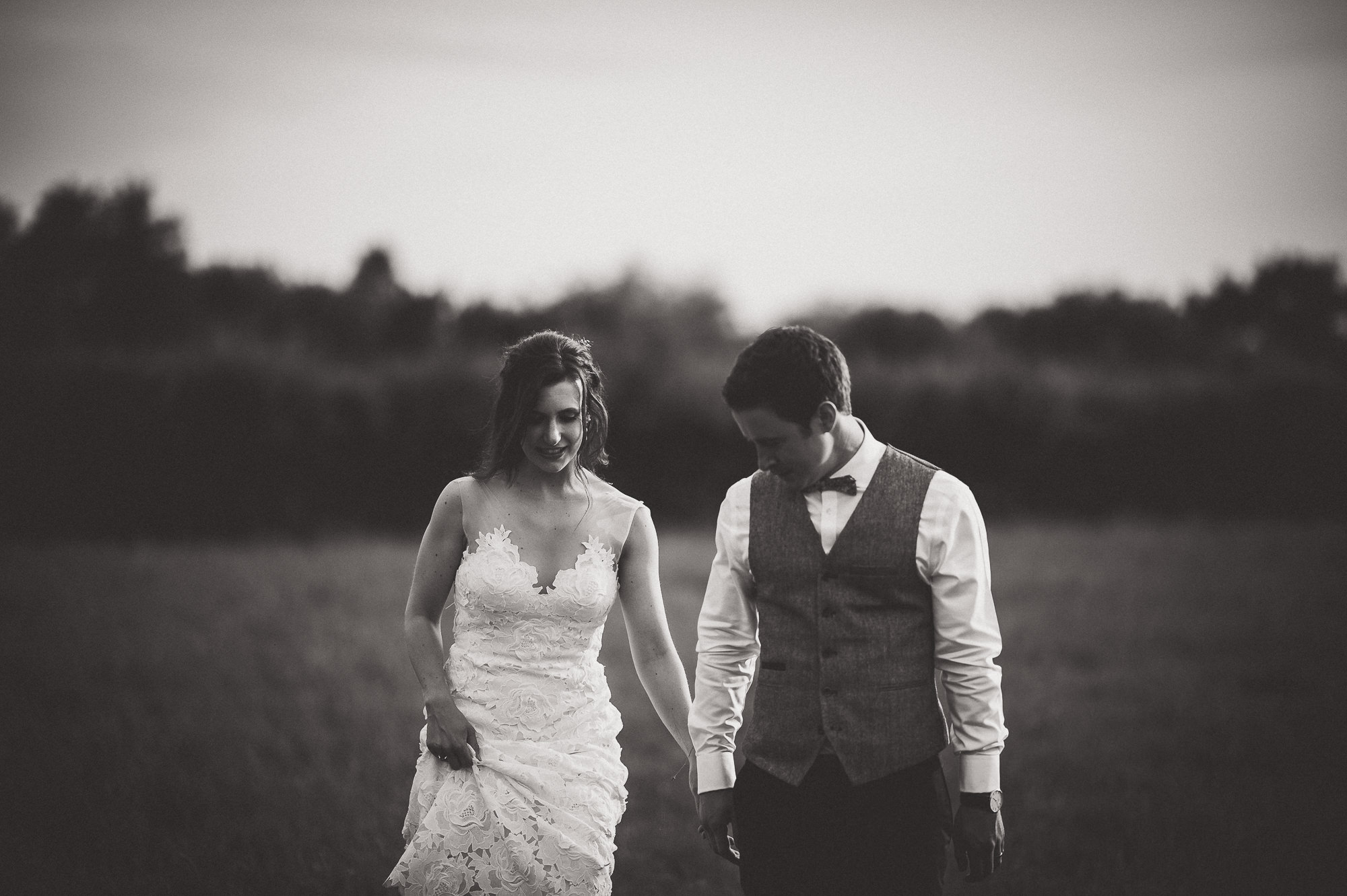 A groom and bride, captured in a lovely wedding photo, strolling through a scenic field.