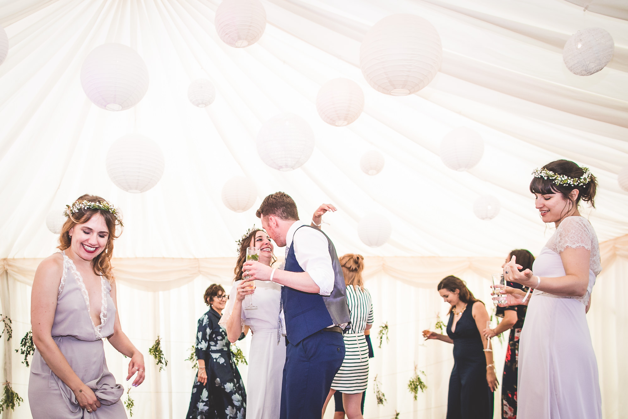 A group of people dancing in a white tent at a wedding celebration.