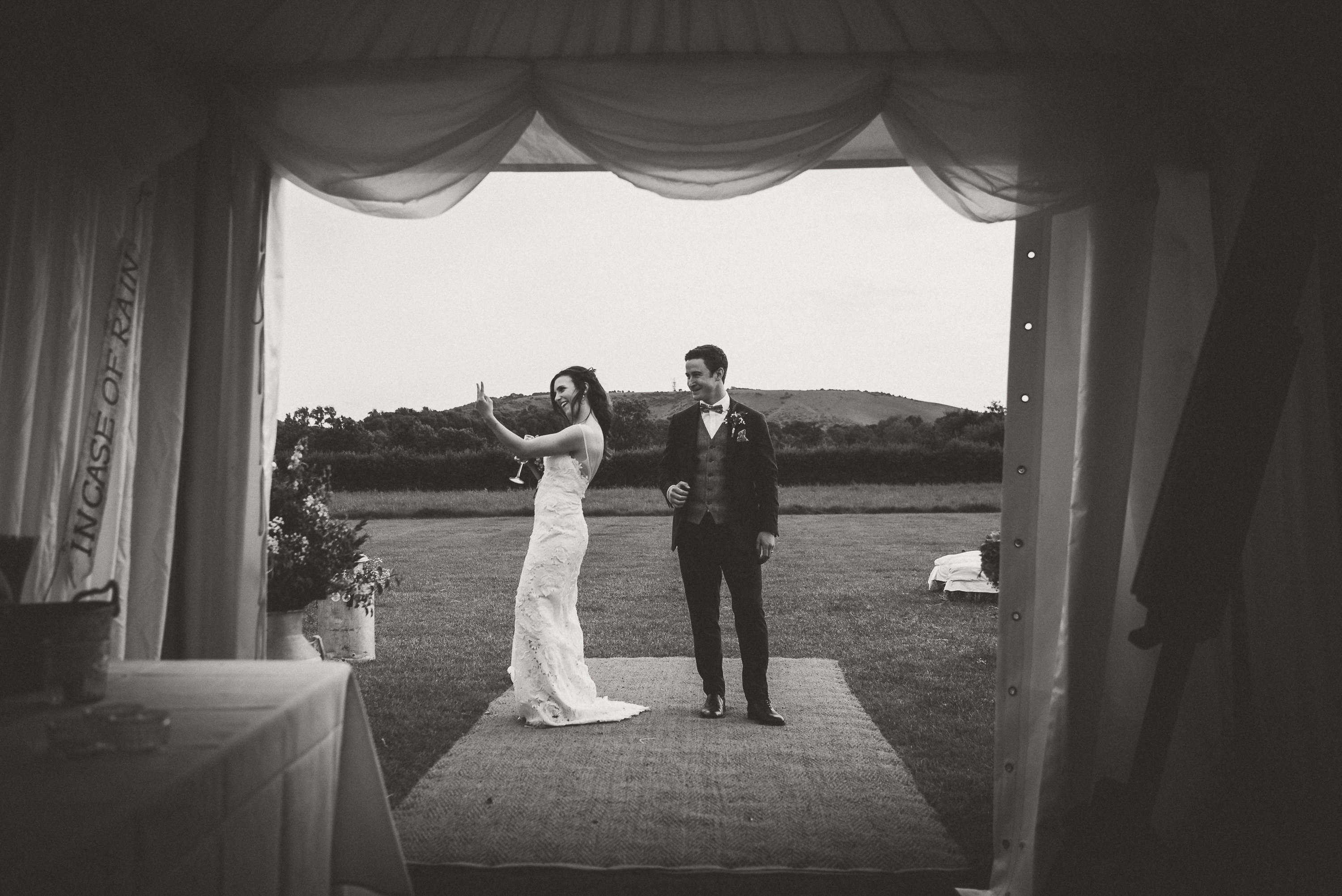 A wedding photographer captures a bride and groom in front of a tent.