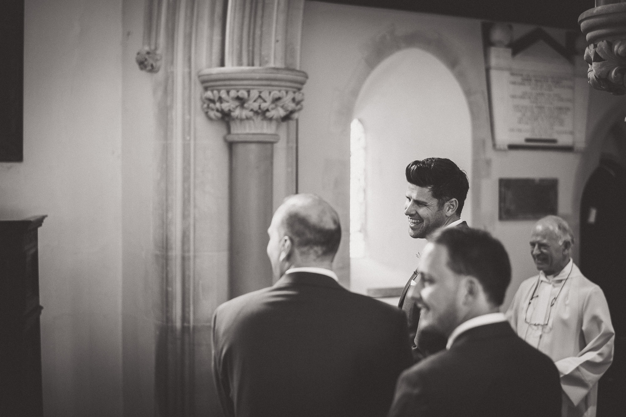 A groom in a suit is standing in front of a church.