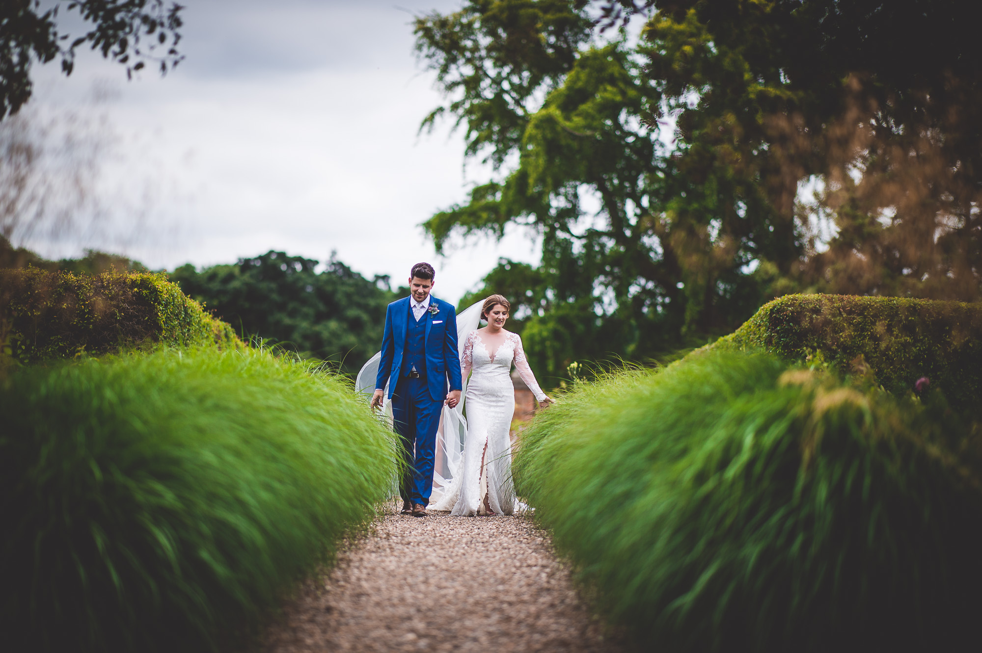 A wedding photographer captures a couple's memorable walk through tall grass at their wedding.