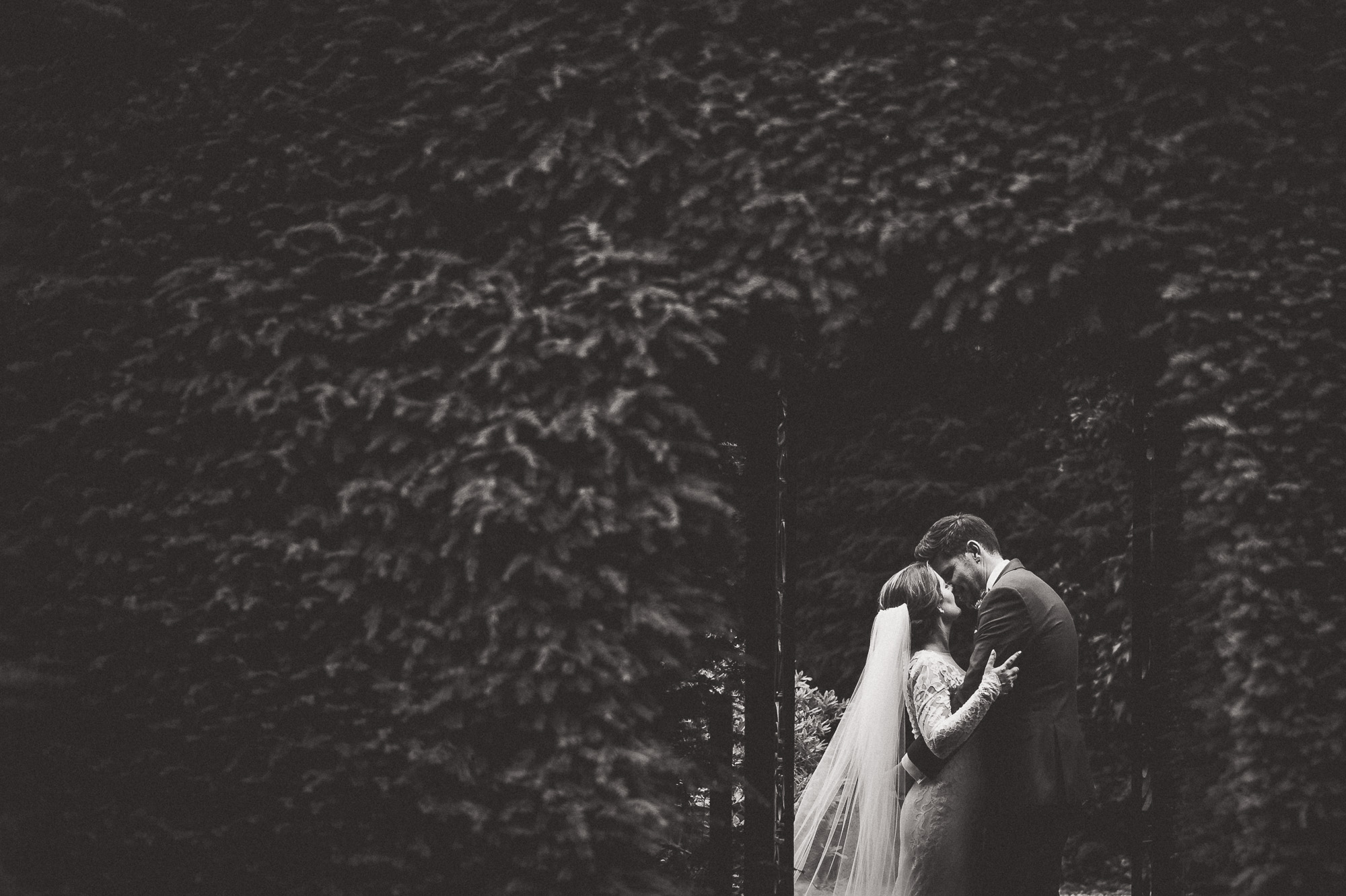 A wedding photo of a bride and groom kissing beneath an ivy covered archway, captured by a skilled wedding photographer.