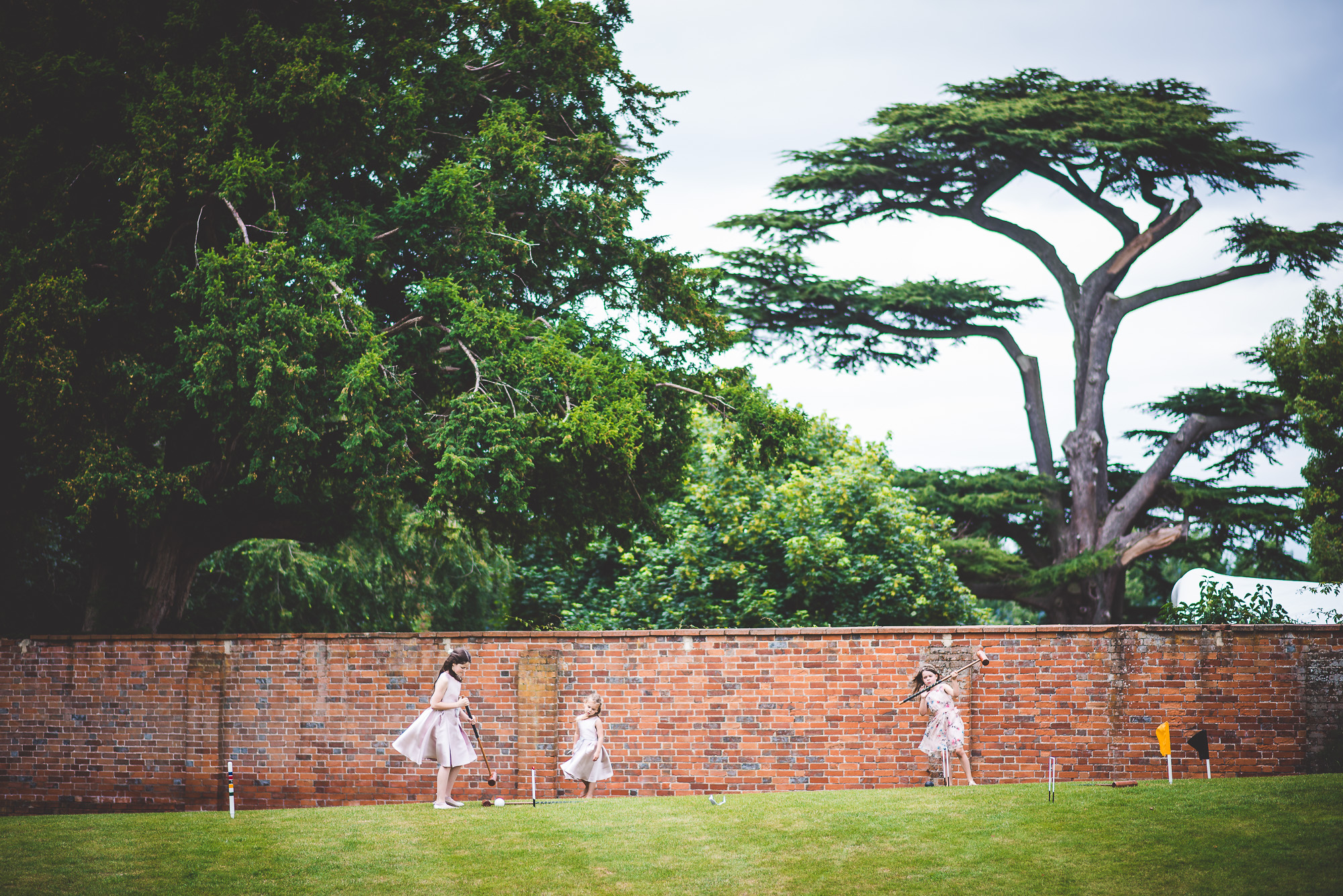A group of girls are playing a game of croquet in front of a brick wall for a wedding photo.