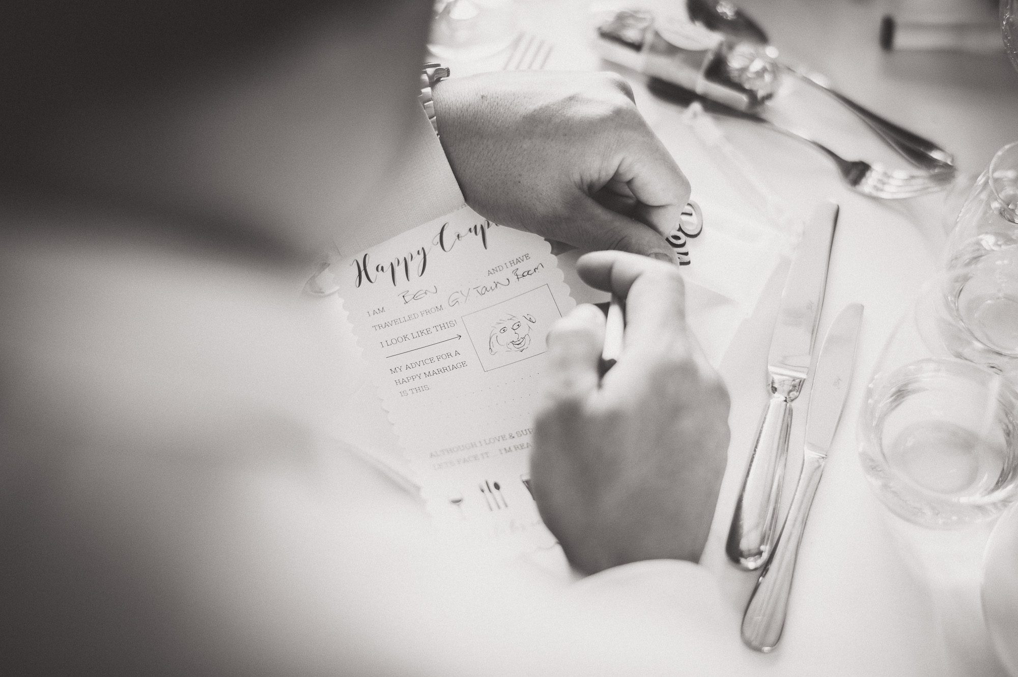 A black and white photo of a groom writing on a piece of paper.