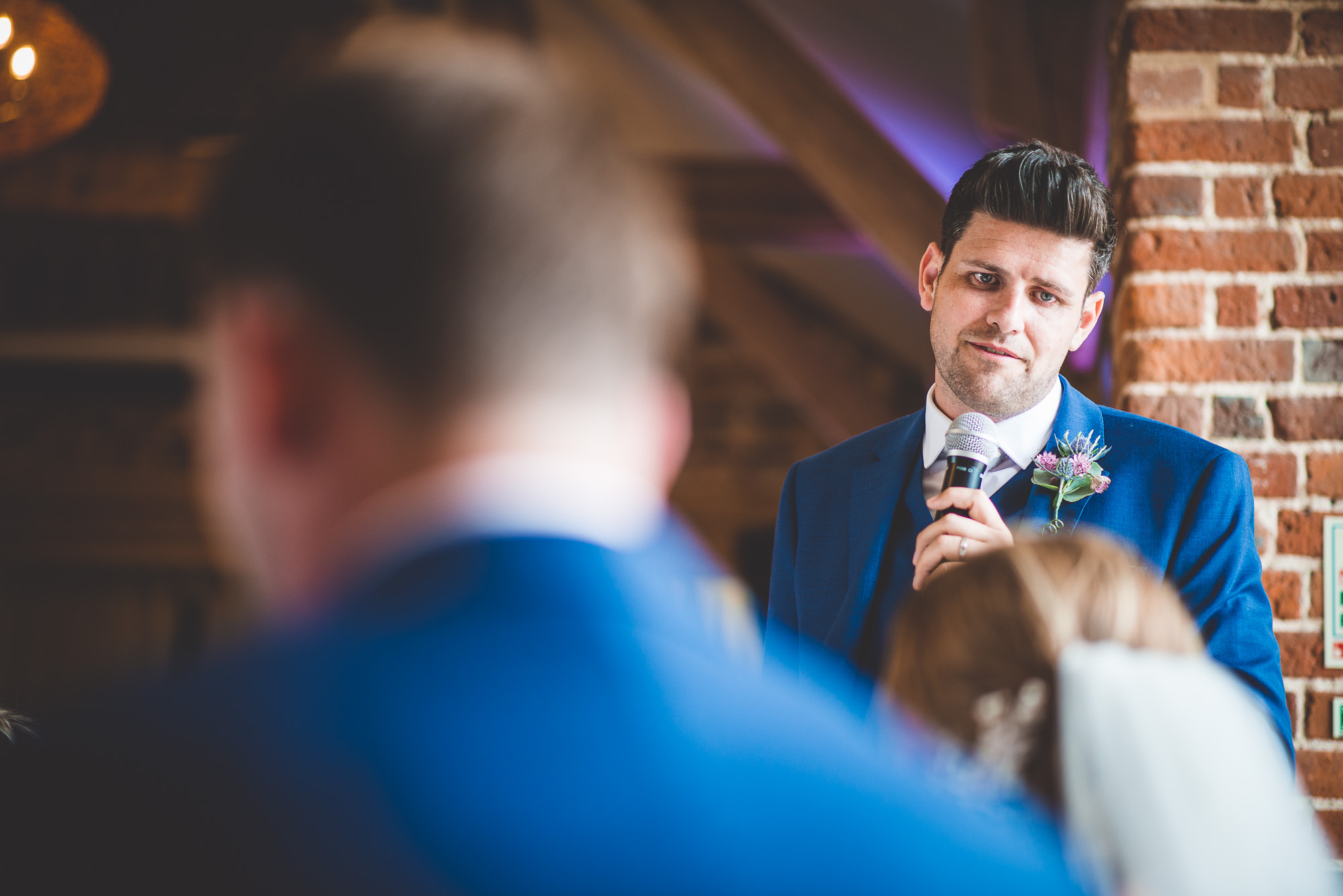 A groom in a blue suit giving a speech at a wedding.