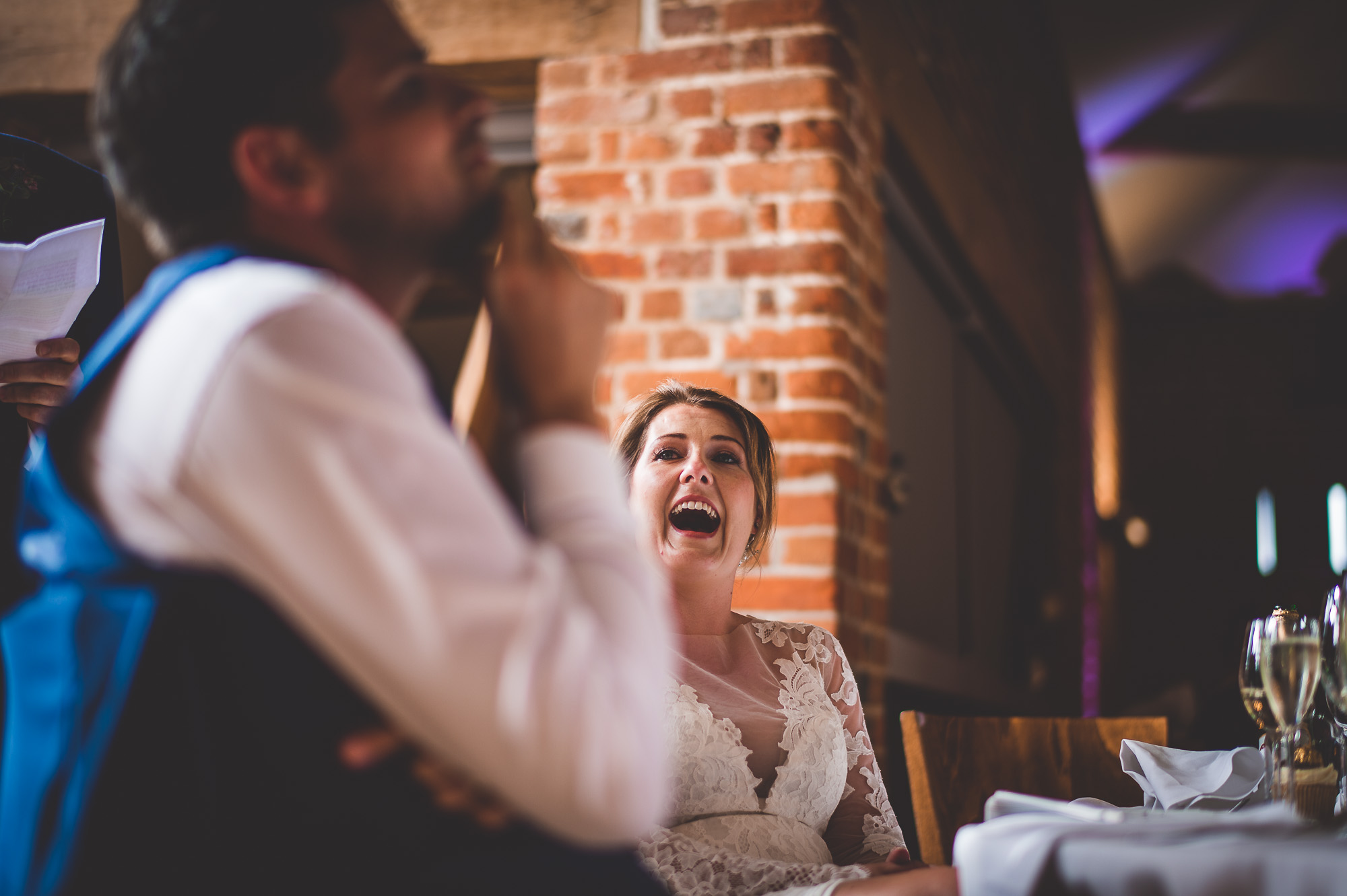 A wedding photographer captures the bride and groom laughing during their speech.