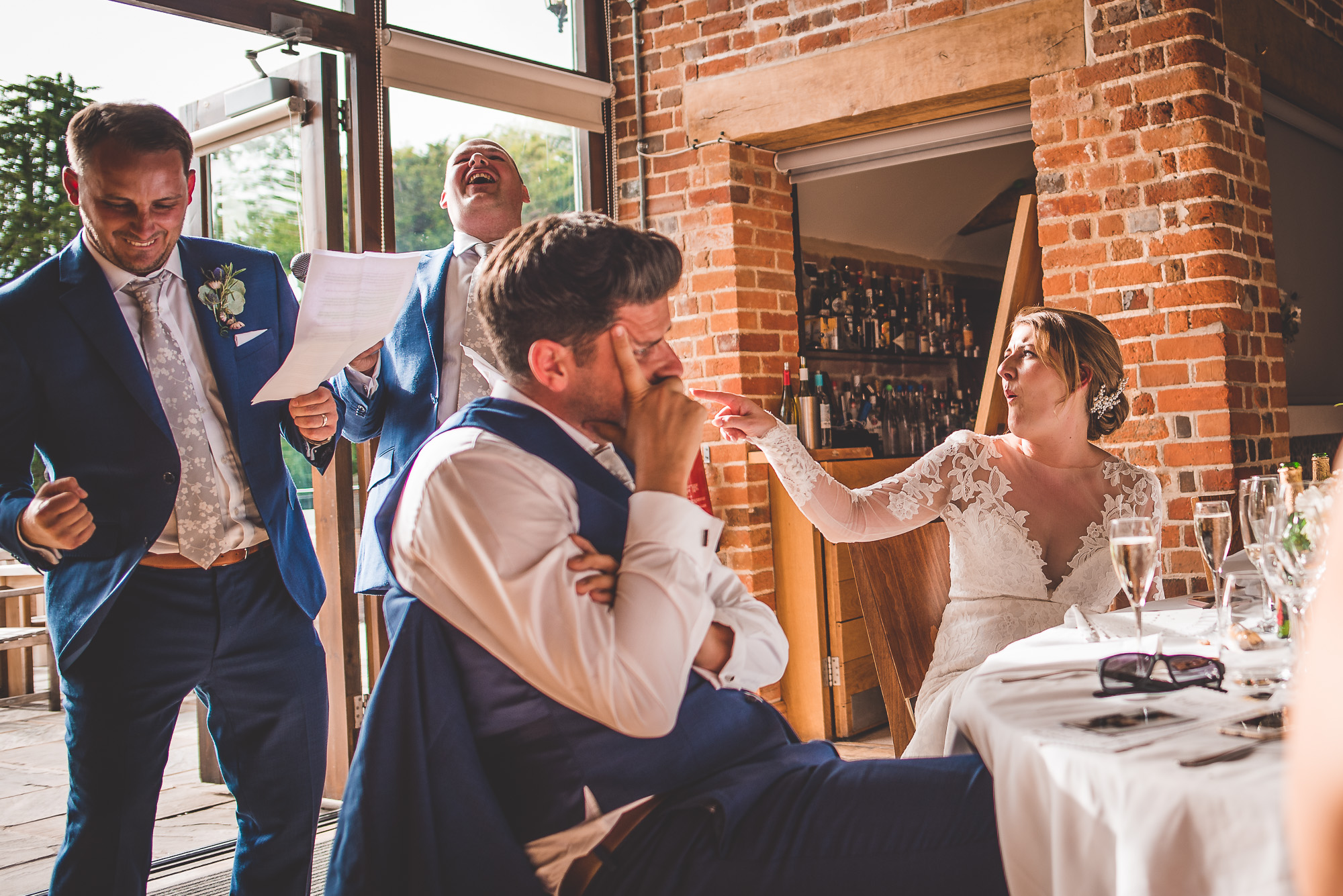A wedding photographer captures the joyous moment of a bride and groom laughing during their speech at a wedding.