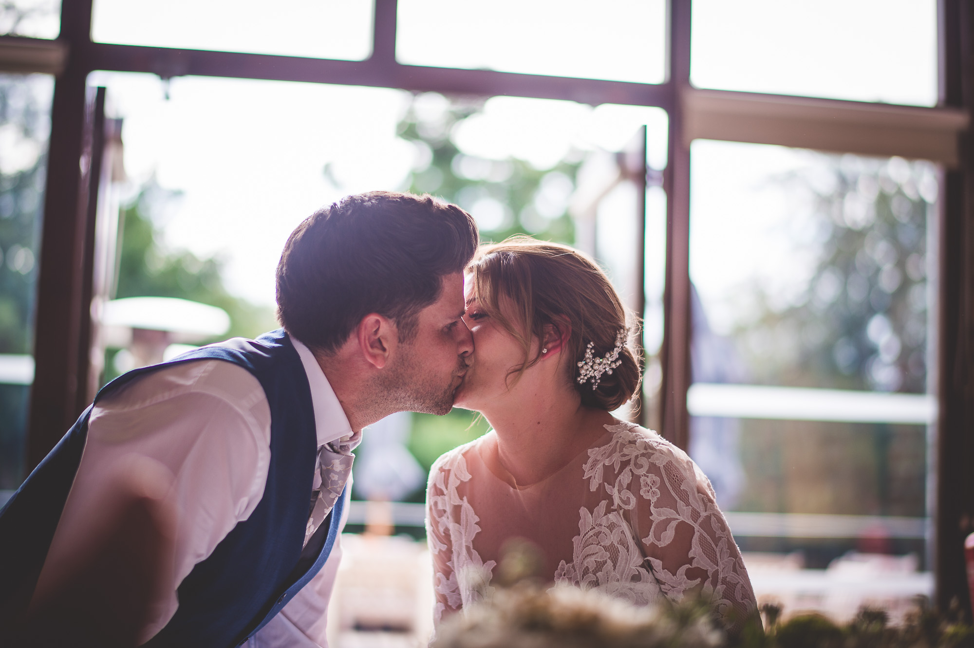A groom and bride sharing a kiss in front of a wedding window.
