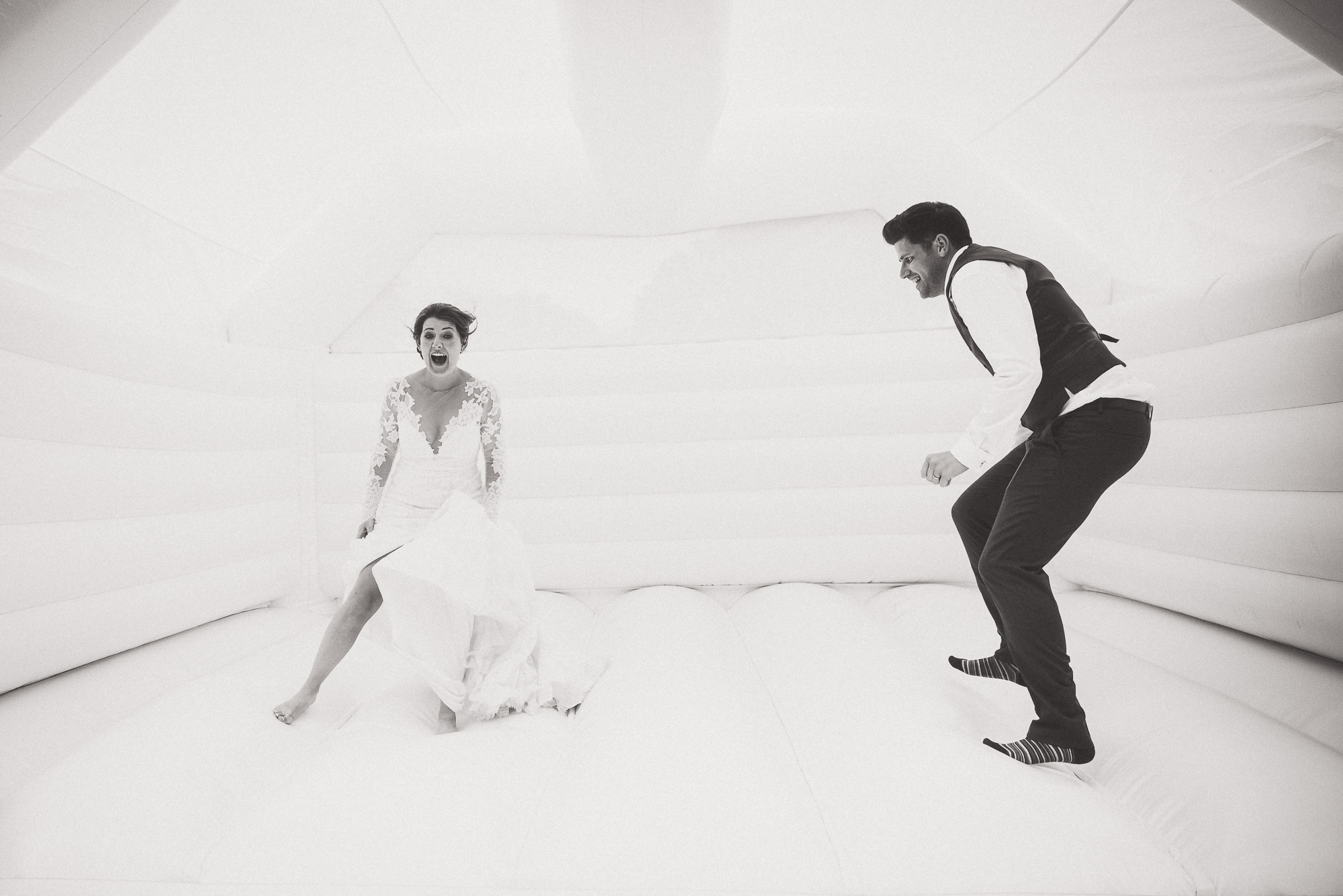A bride and groom happily jumping in an inflatable bouncy castle for a memorable wedding photo.