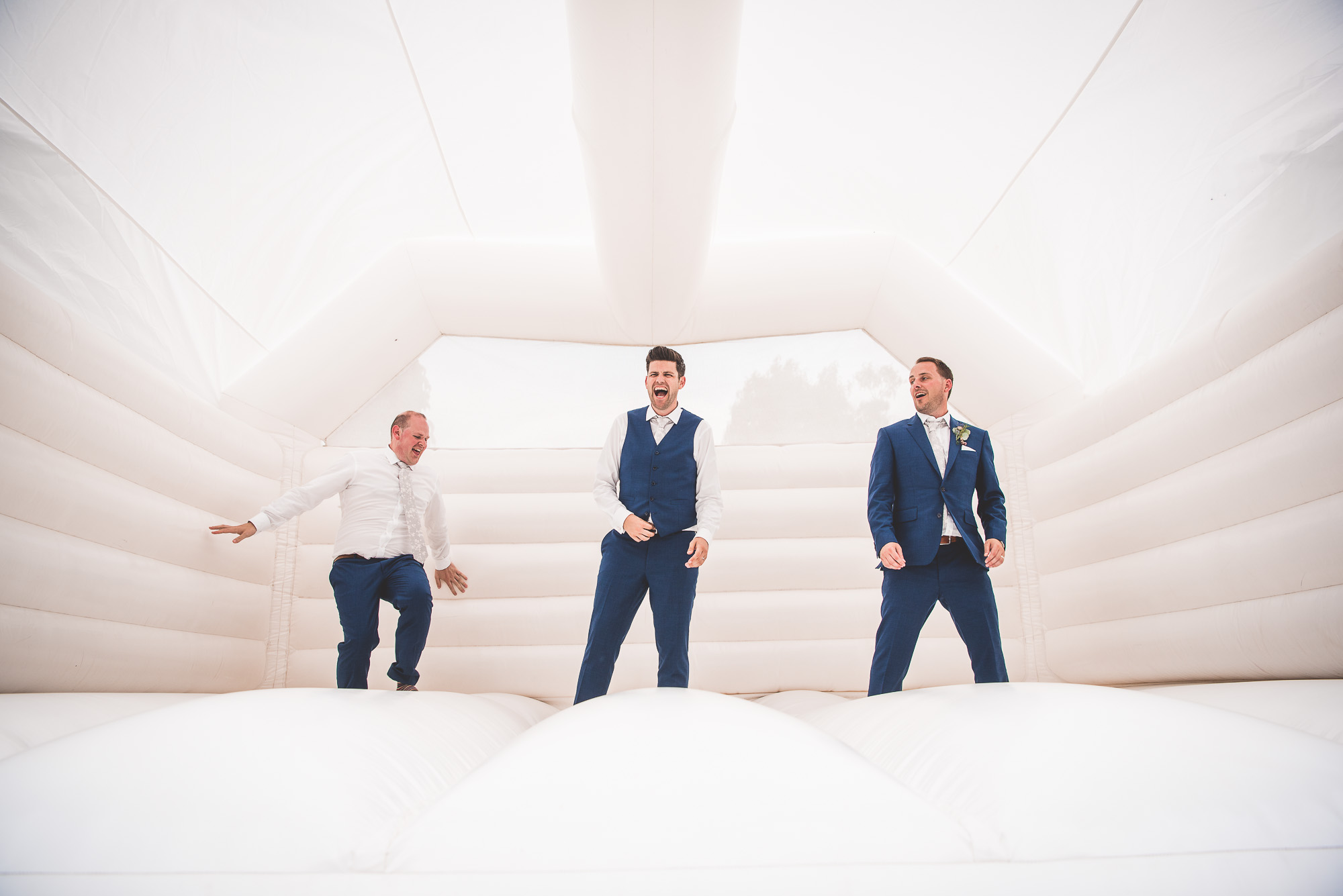 A bride's wedding photo featuring three groomsmen on an inflatable bouncy castle, captured by a wedding photographer.