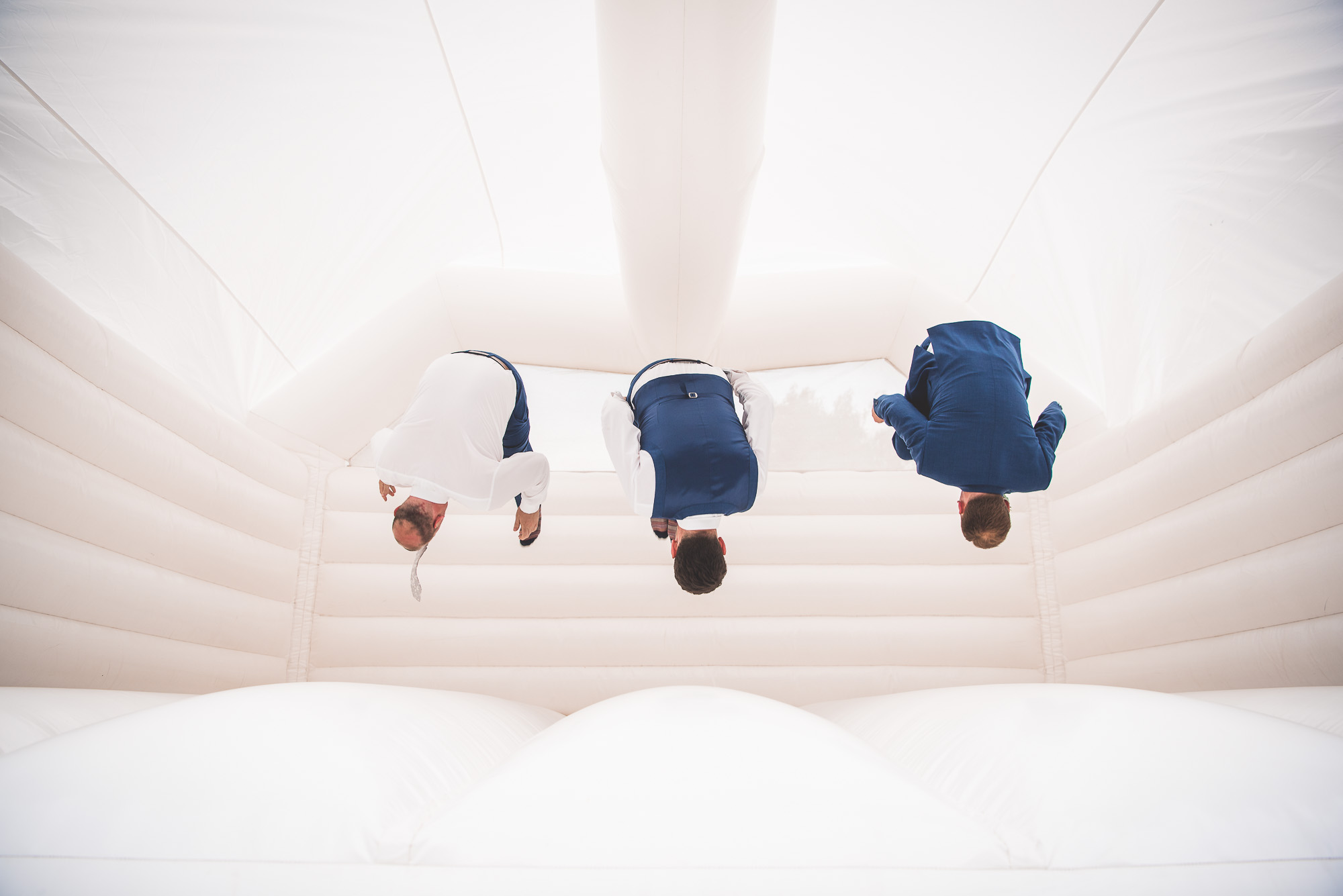 A group of groomsmen in suits posing on top of a white inflatable for their wedding photographer.