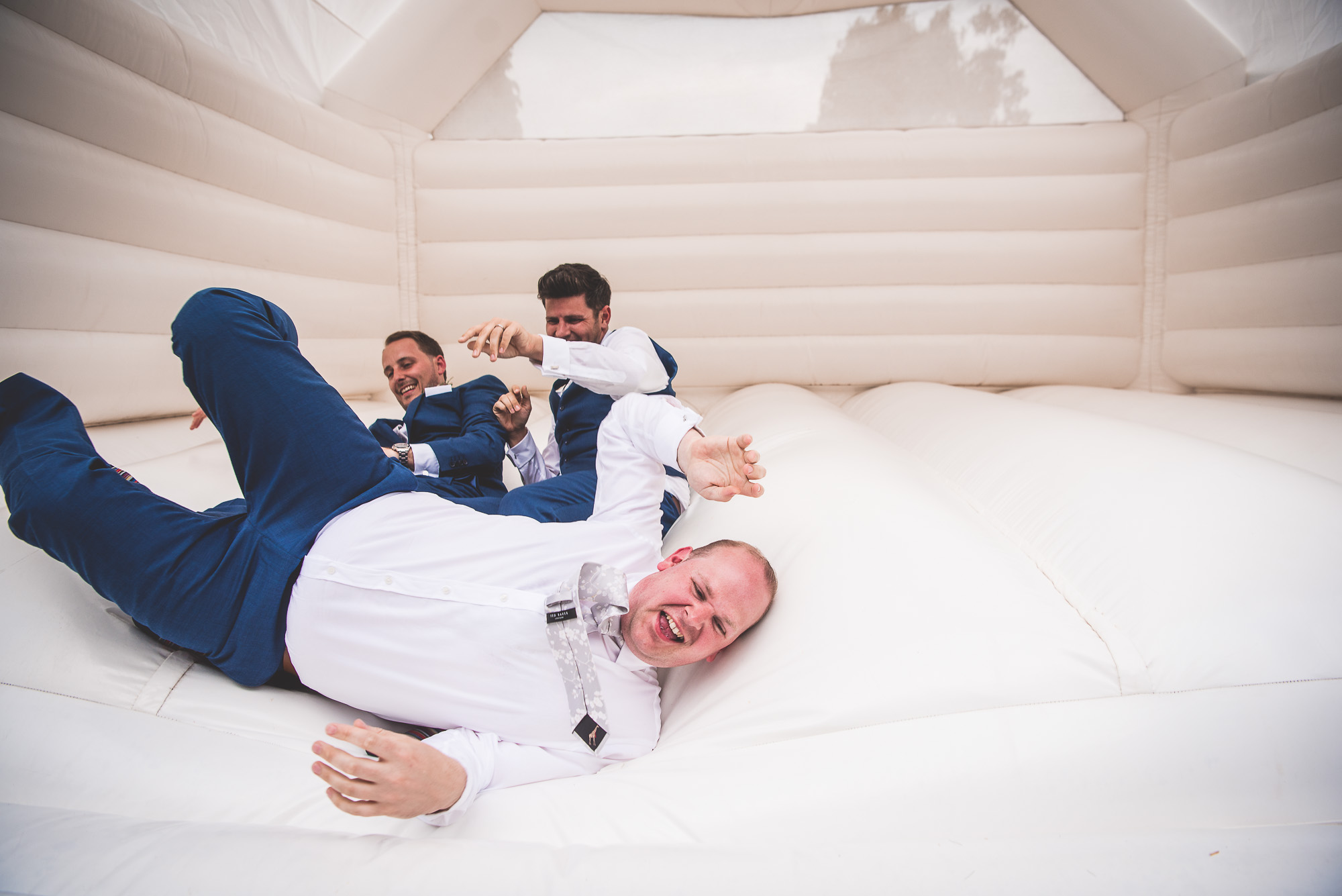 Groomsmen lounging on an inflatable bouncer at a wedding celebration.