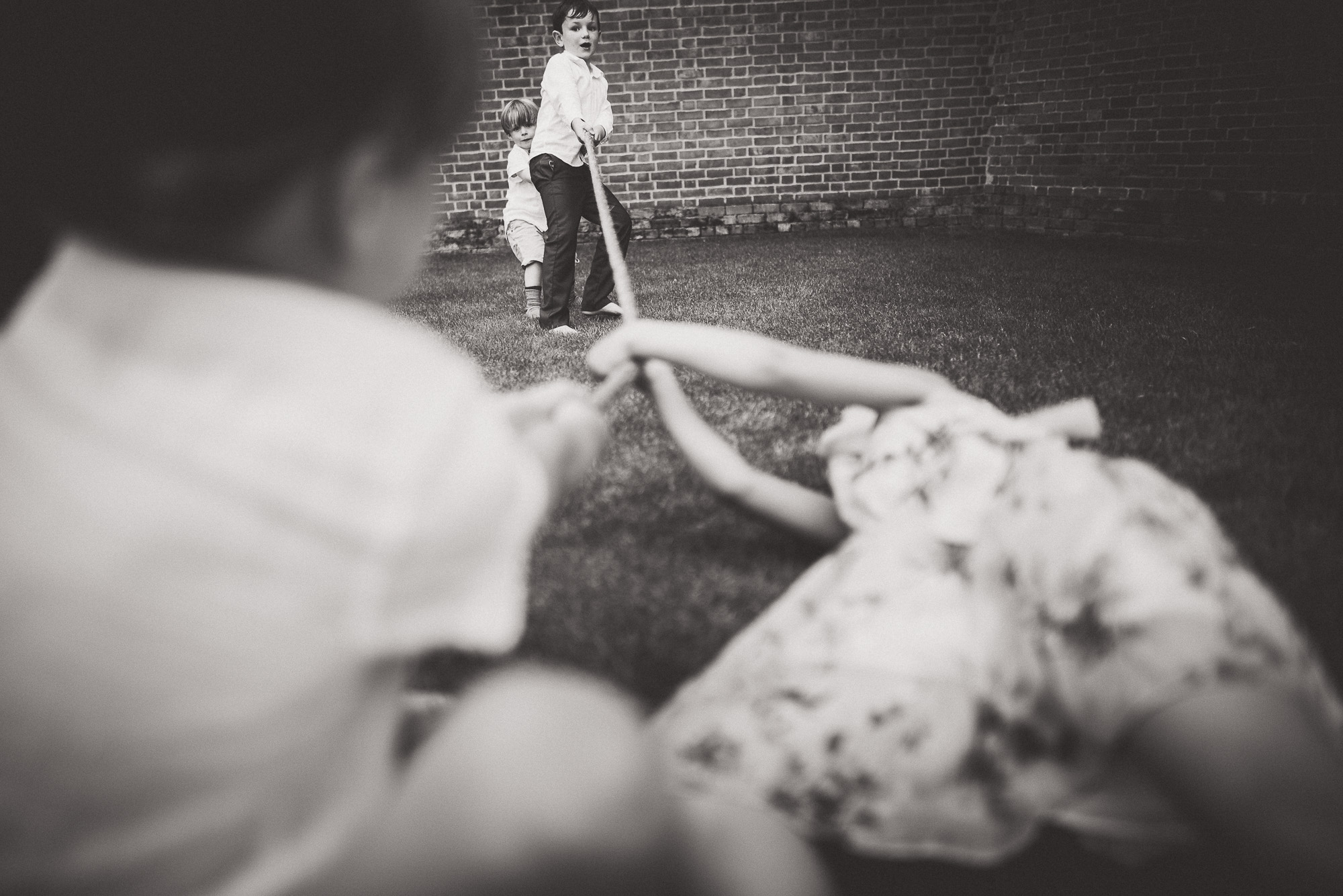 A black and white photo of two children playing in the grass, captured by a wedding photographer.