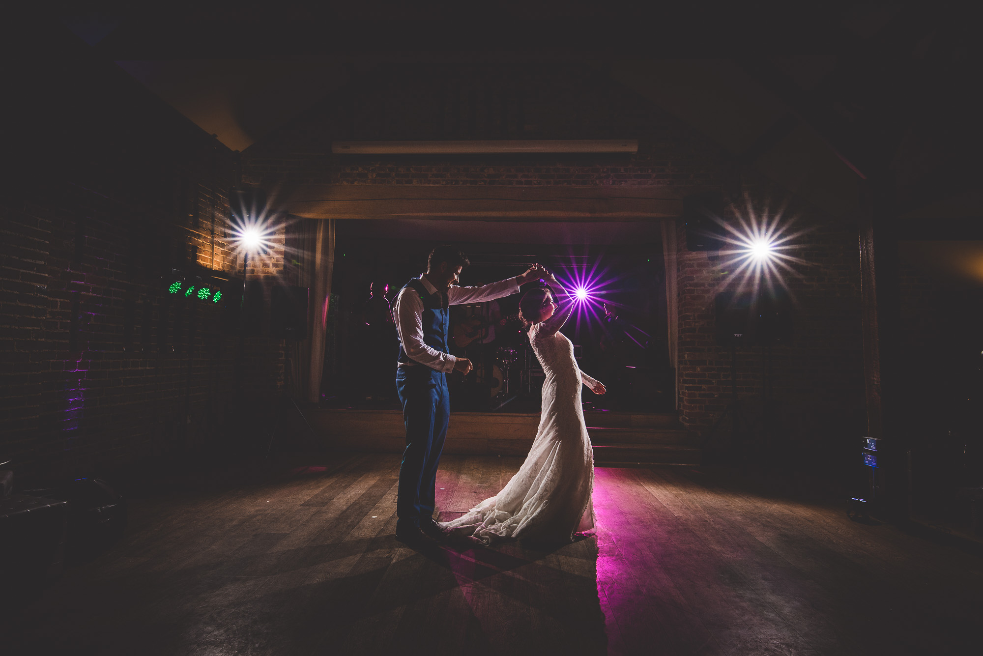 A wedding photographer captures a bride and groom dancing in a dark room.