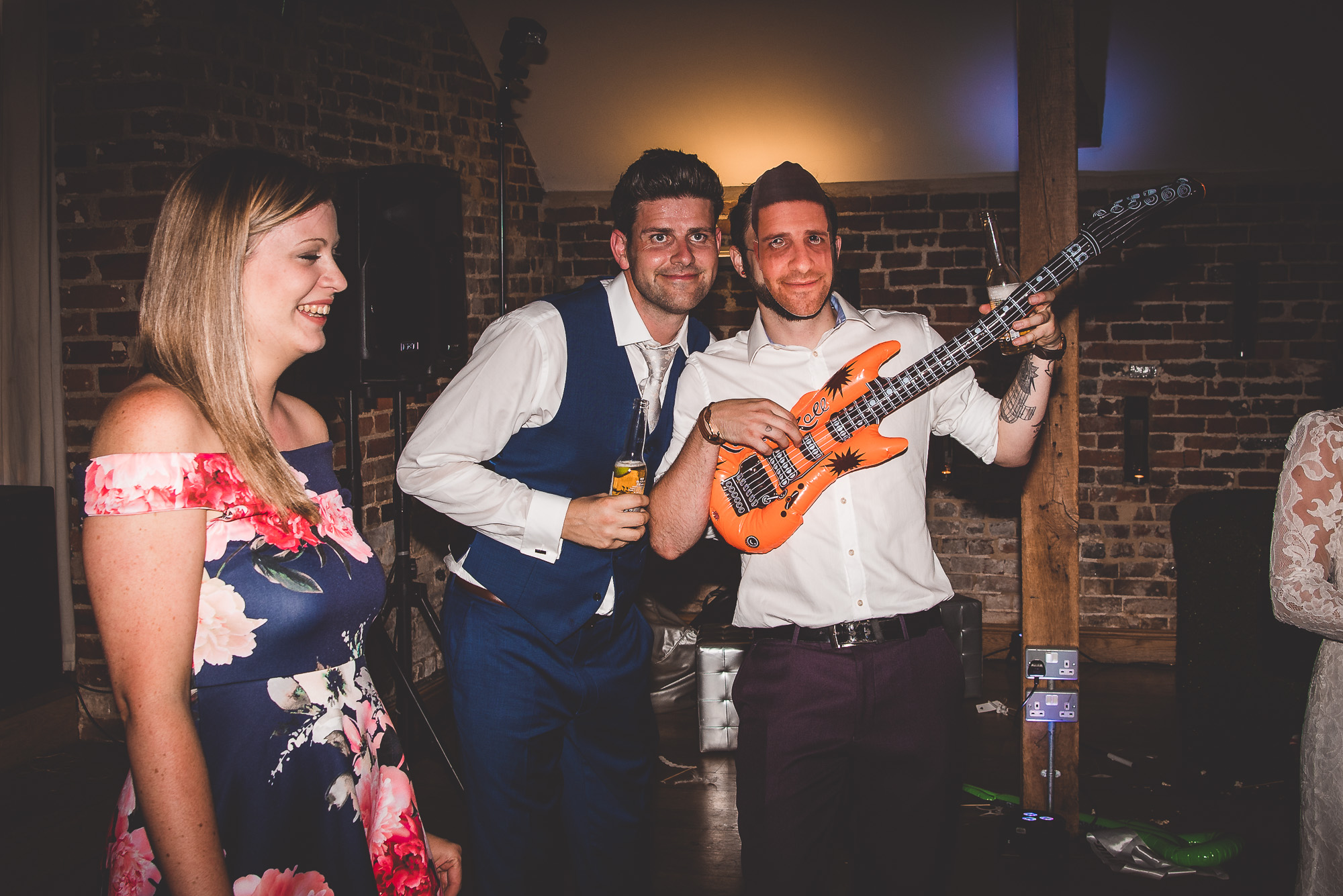 A group of people including the groom and bride holding a guitar at their wedding reception.