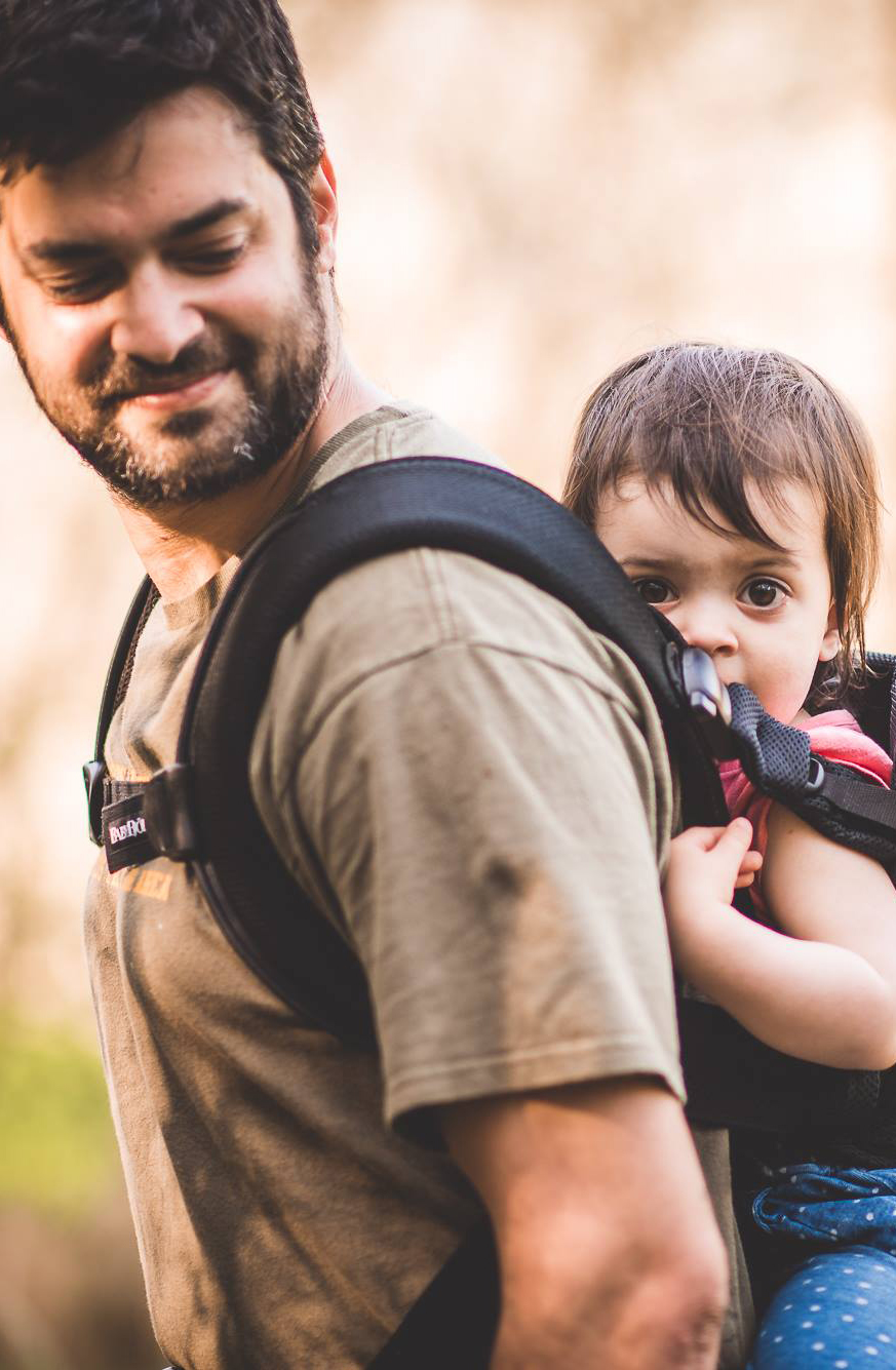 A groom holding a baby in a baby carrier at a wedding.