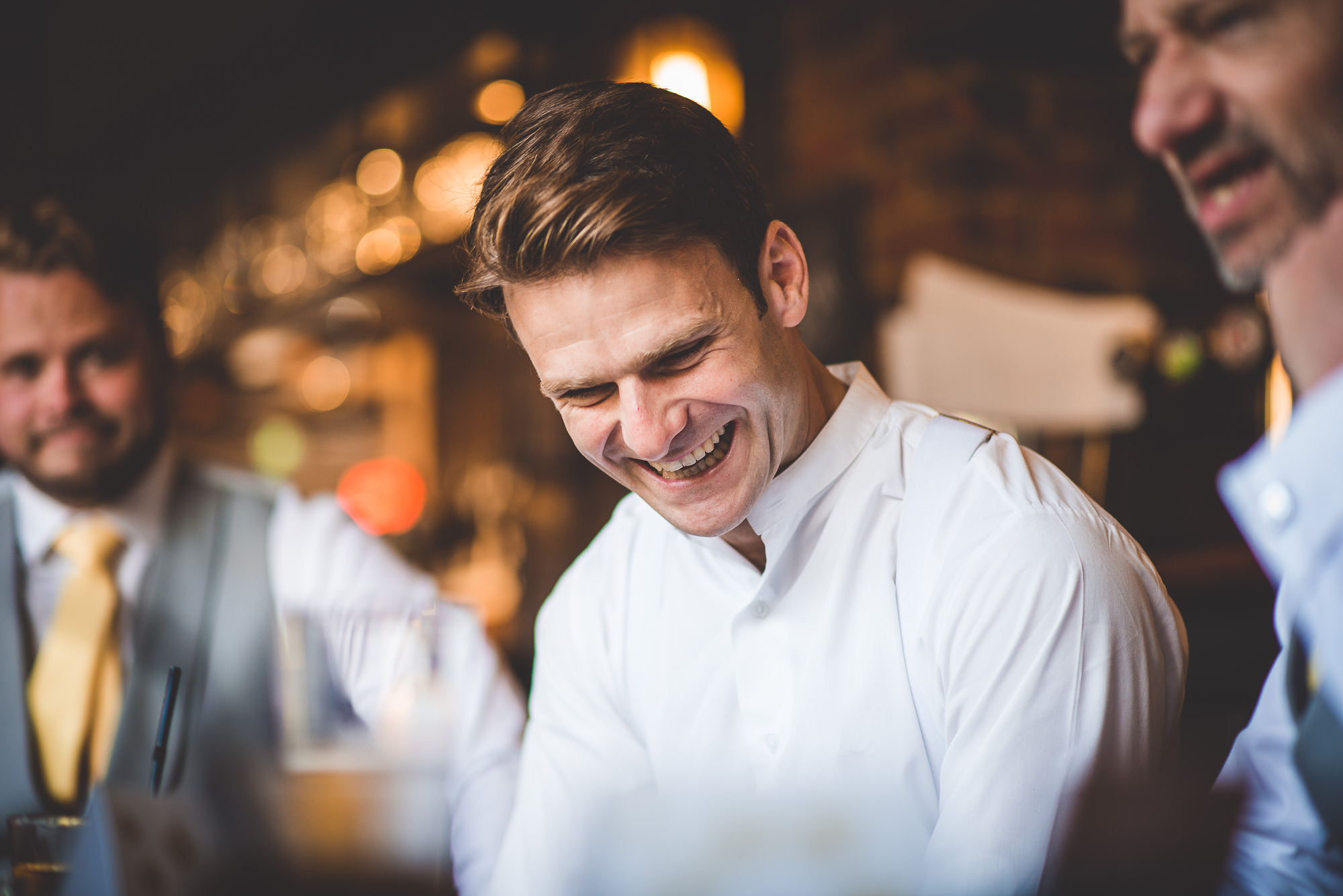 A group of men, including the groom, laughing at a bar during the wedding reception.