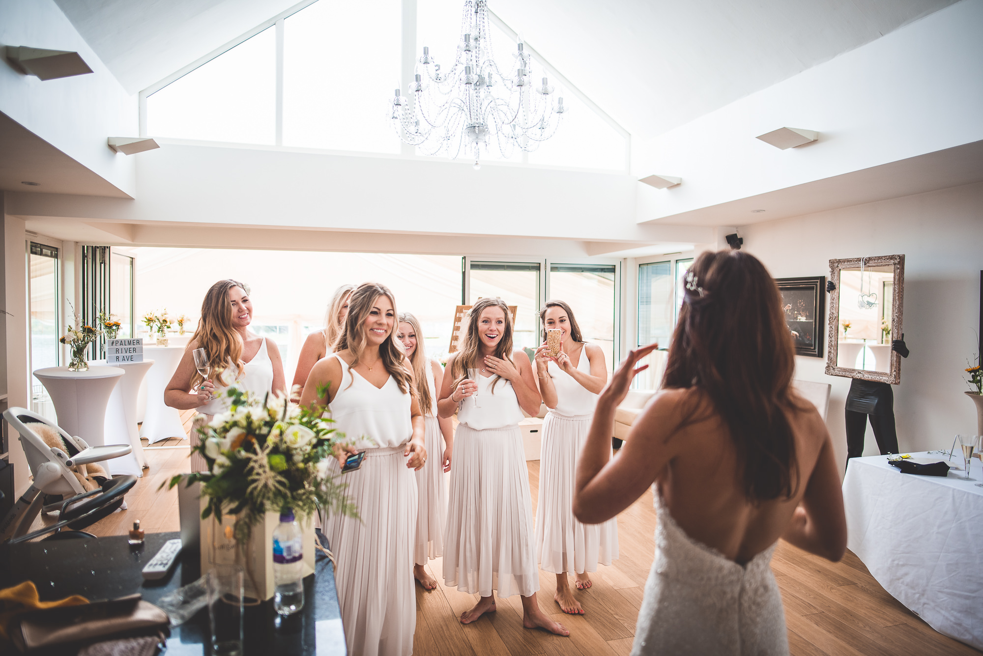 A bride and her bridesmaids, captured by a wedding photographer, stand elegantly in front of a grand chandelier.