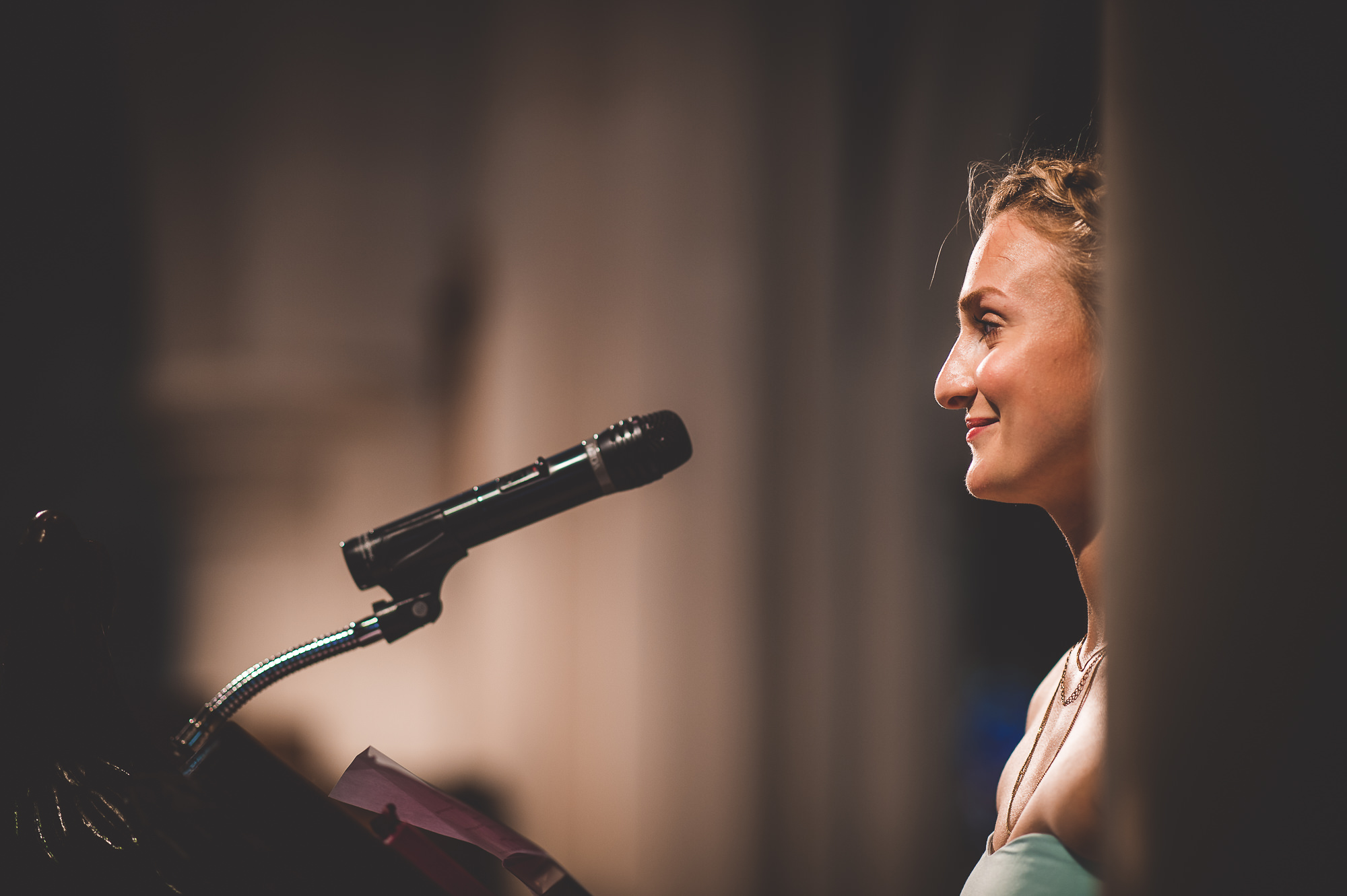 A wedding photographer captures a woman speaking into a microphone during a wedding ceremony.