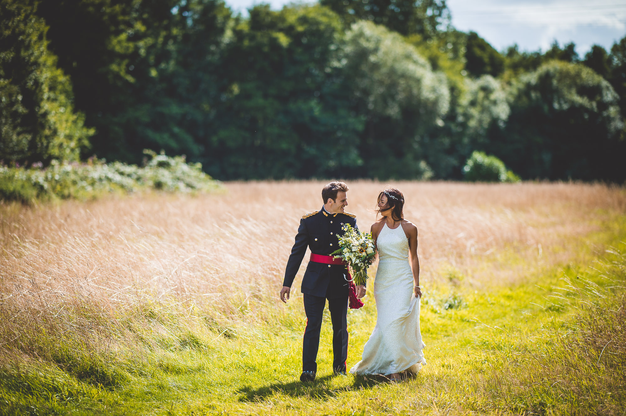A wedding photographer captures a bride and groom in a field of tall grass, creating a stunning wedding photo.