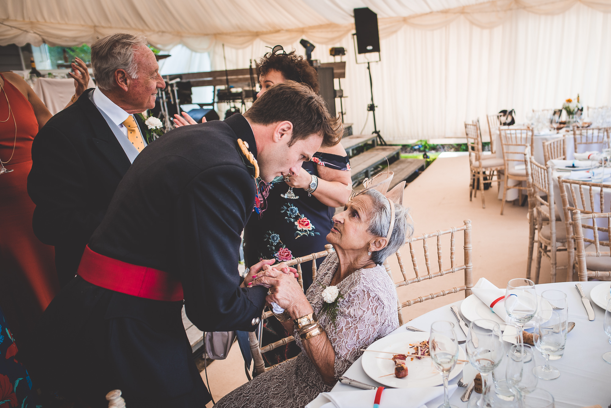 A groom in a suit is giving a bride a drink at the wedding.