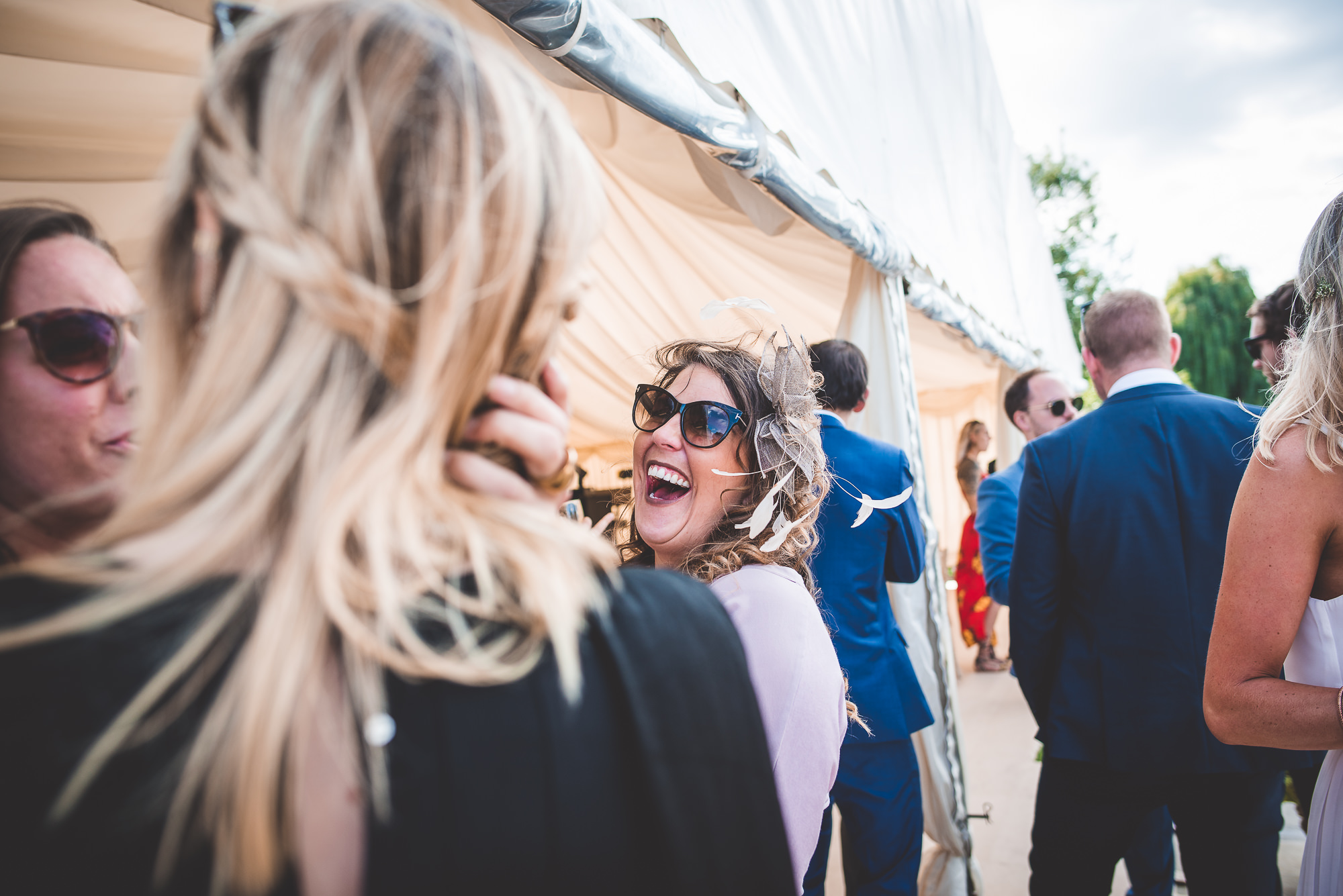 A group of people, including the groom, posing for a wedding photo inside a tent while being captured by a wedding photographer.