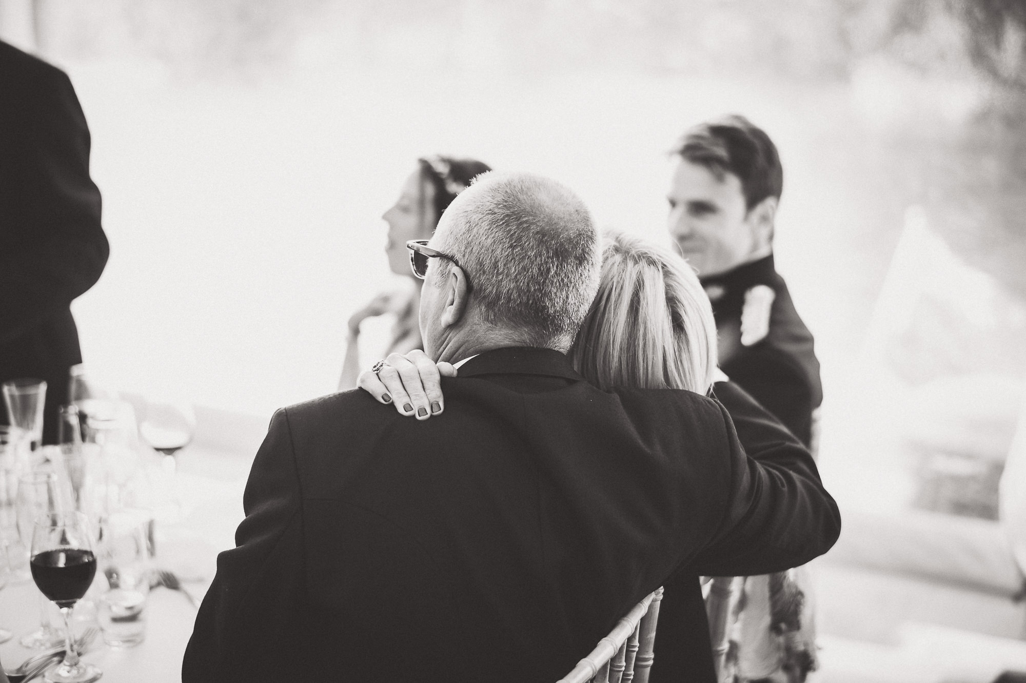 A black and white wedding photo capturing a groom hugging his bride.