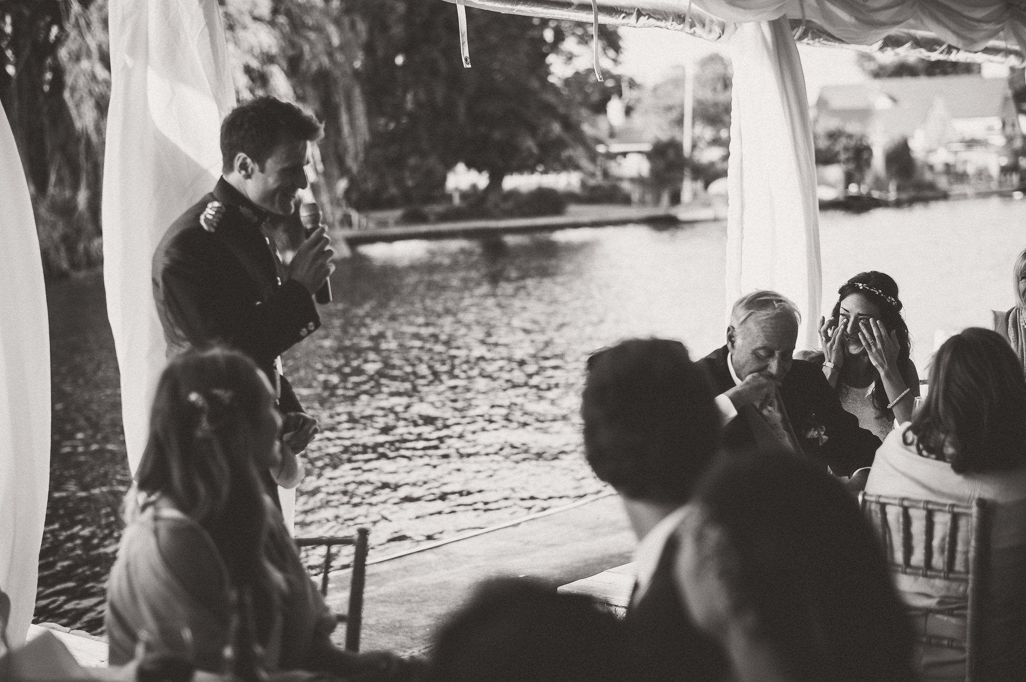 A black and white wedding photo capturing a man giving a speech.