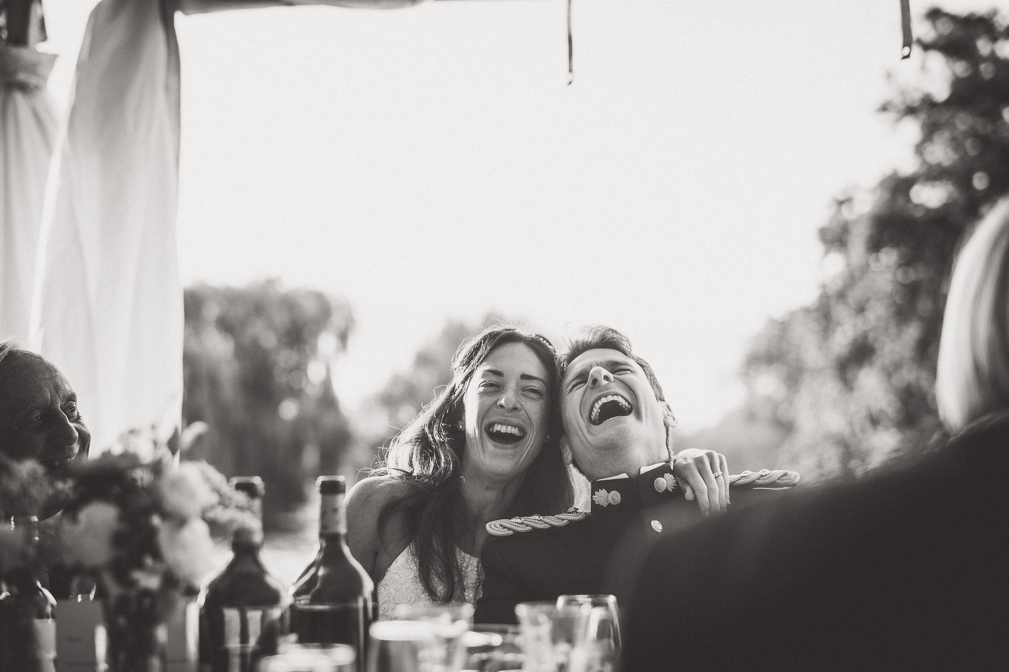 A wedding photographer captures a joyful wedding photo of the bride and groom laughing at their reception.