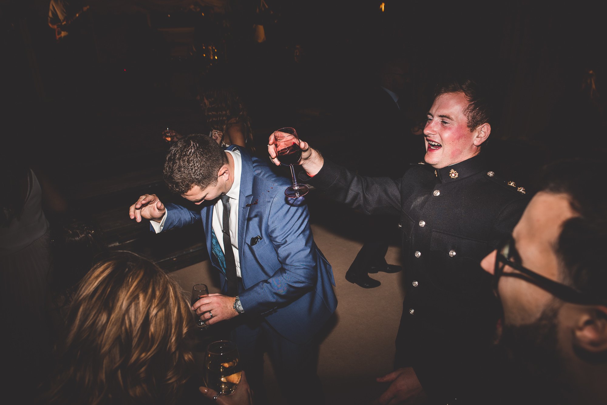 A wedding photographer captures a man in a suit sipping wine at the wedding party.