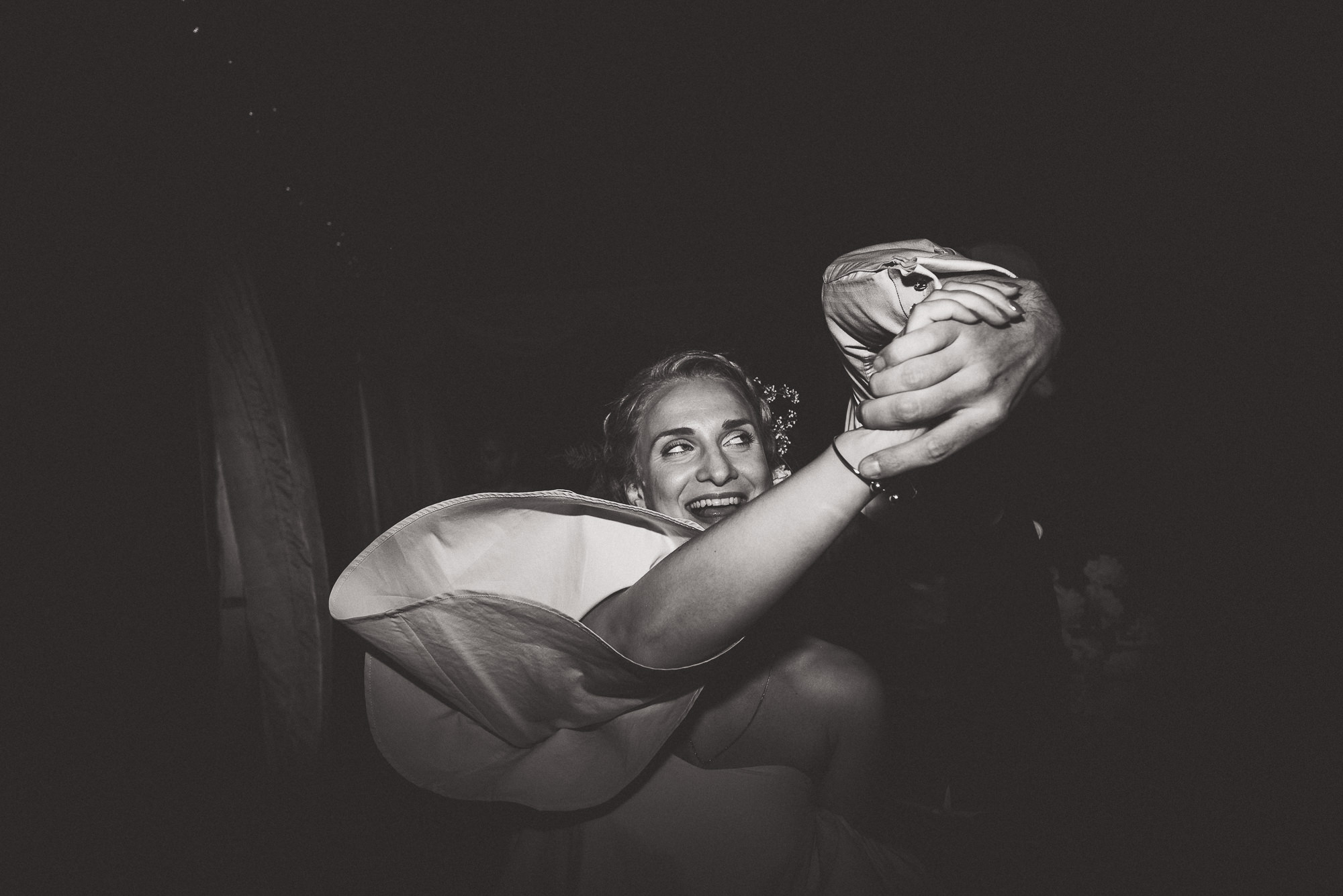 A black and white photo of a woman dancing in a dark room, resembling a bride on her wedding day.